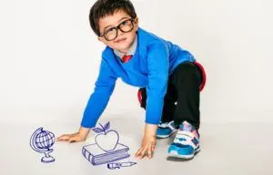 Young boy wearing glasses and a blue sweater crouching on the floor beside playful illustrations of a globe, book, apple, and pencil.