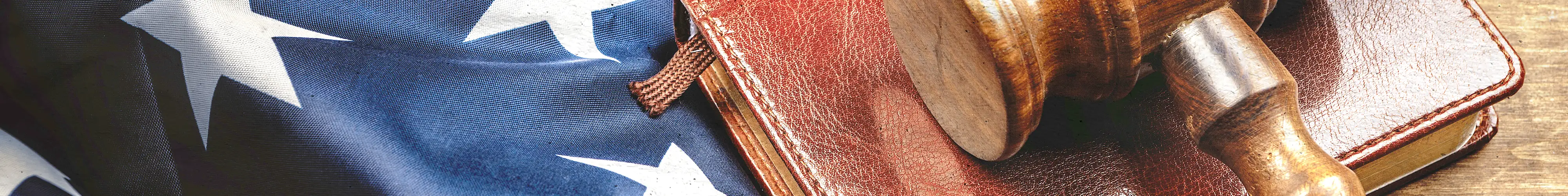 A wooden gavel resting on a leather book beside an American flag.