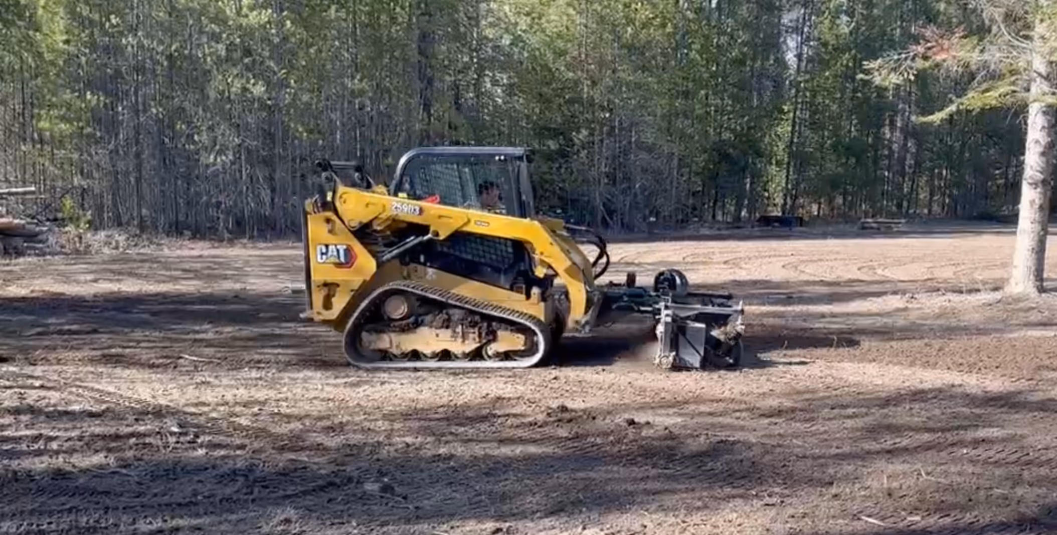 A yellow compact track loader with a power rake attachment.