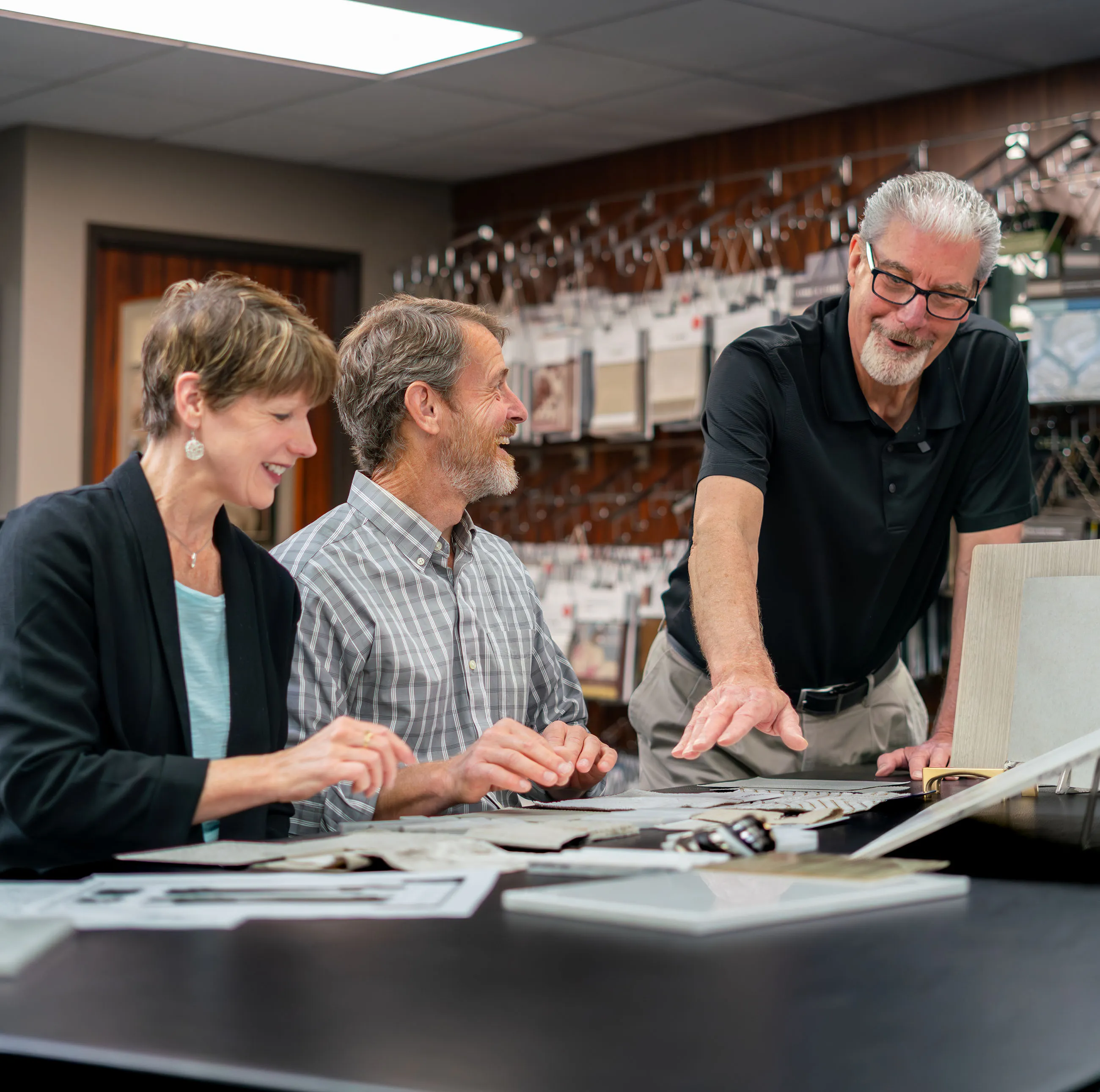 Three adults reviewing interior design fabric samples and materials at a table in a showroom.