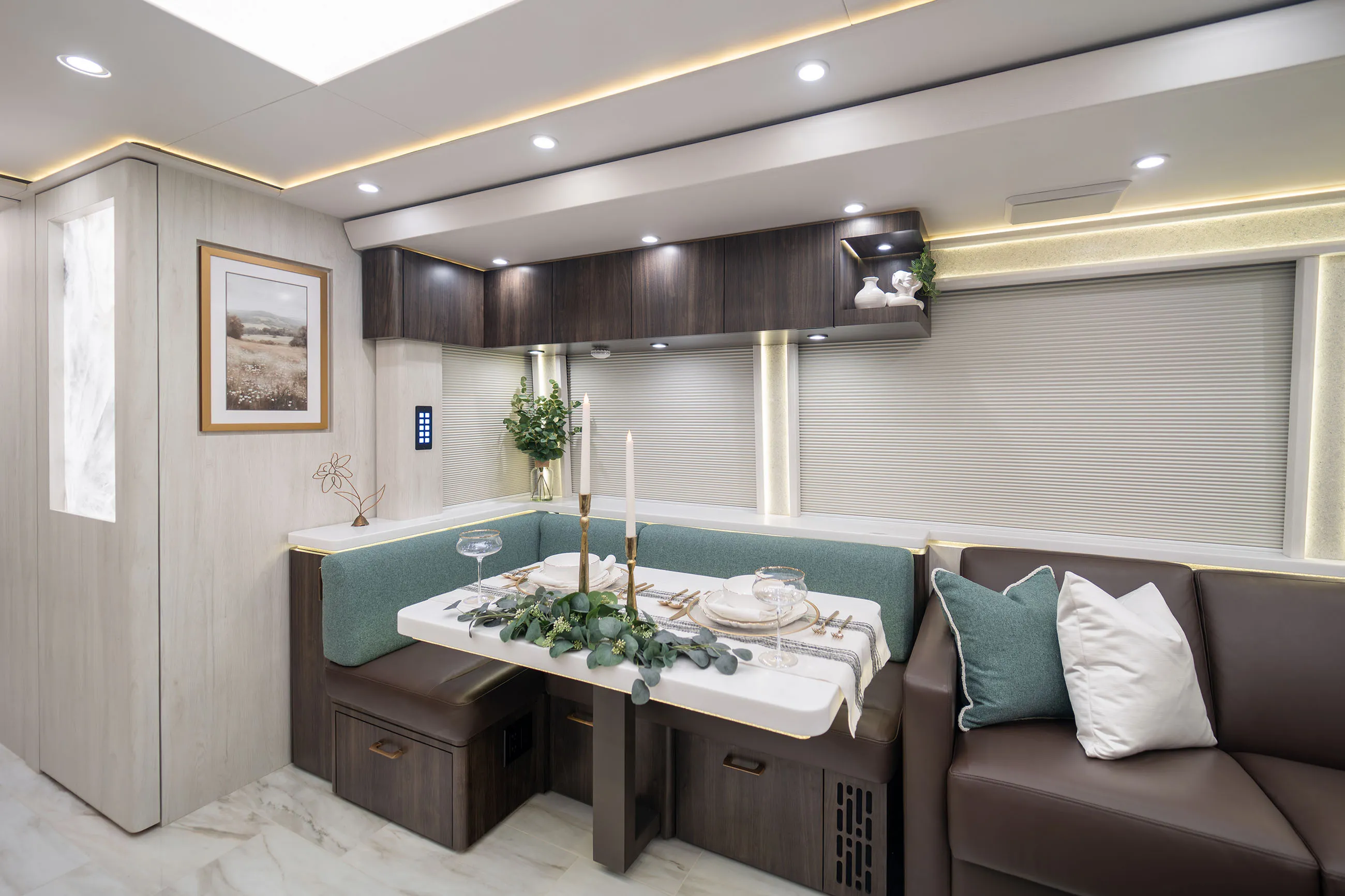 Modern RV dining area with U-shaped teal and brown seating, white table set with gold-rimmed plates, candles, and greenery.