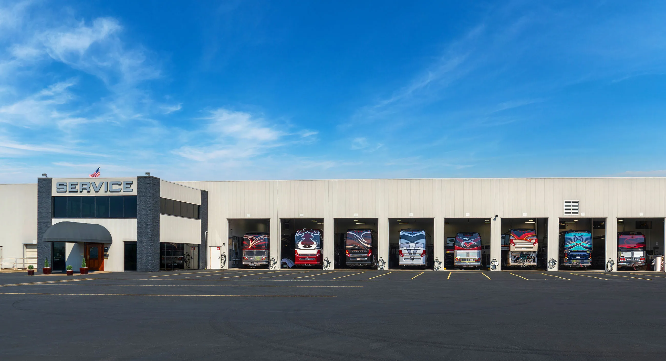 Bus service center with eight buses parked in service bays under a blue sky.