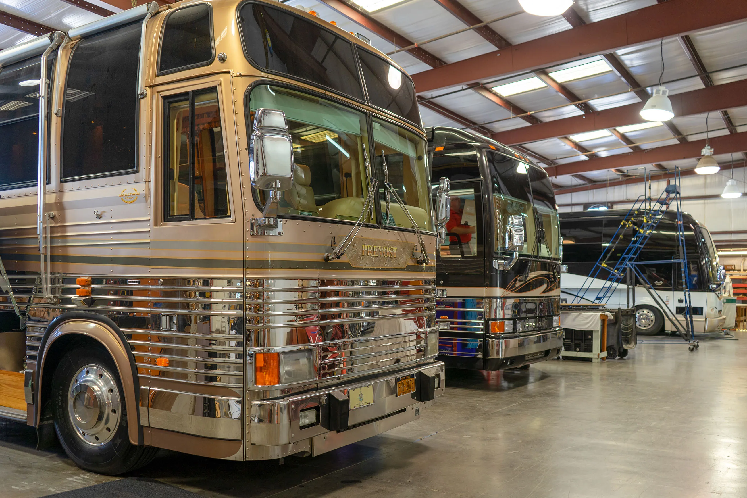 Three parked luxury tour buses inside a spacious maintenance garage.