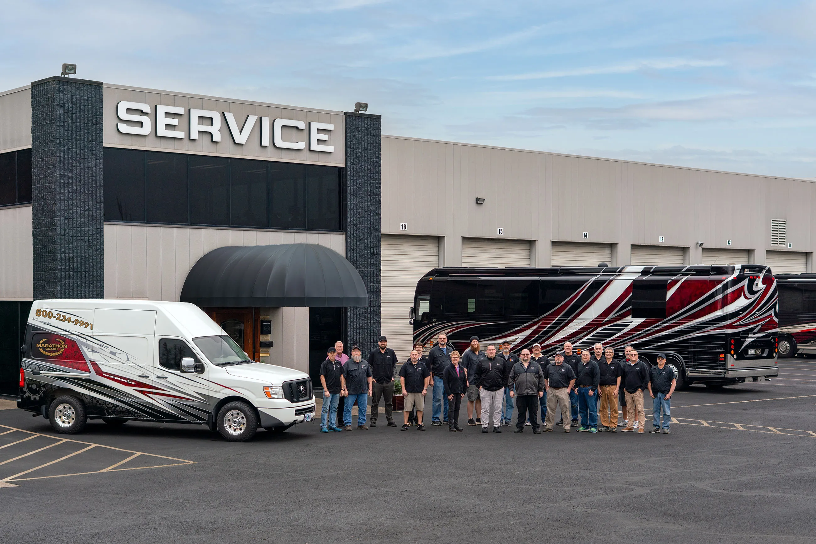 Group of service staff standing in front of a building with SERVICE sign, next to a decorated white service van and a black and red bus.