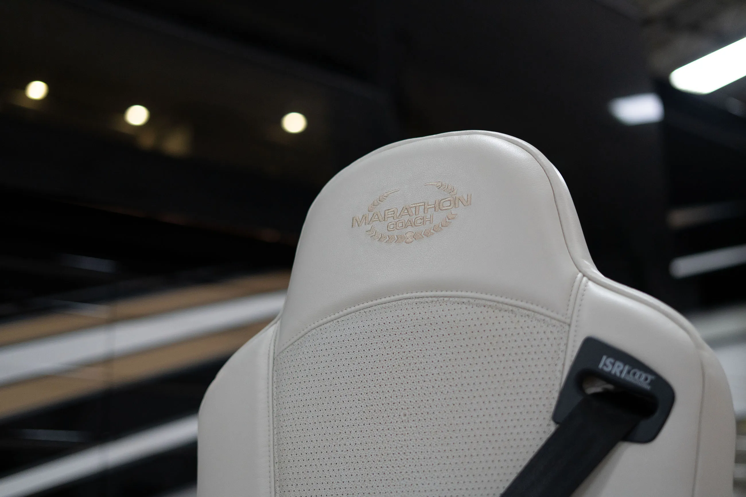 Close-up of a white leather car seat with the embroidered text 'MARATHON COACH' and a black seatbelt attached.