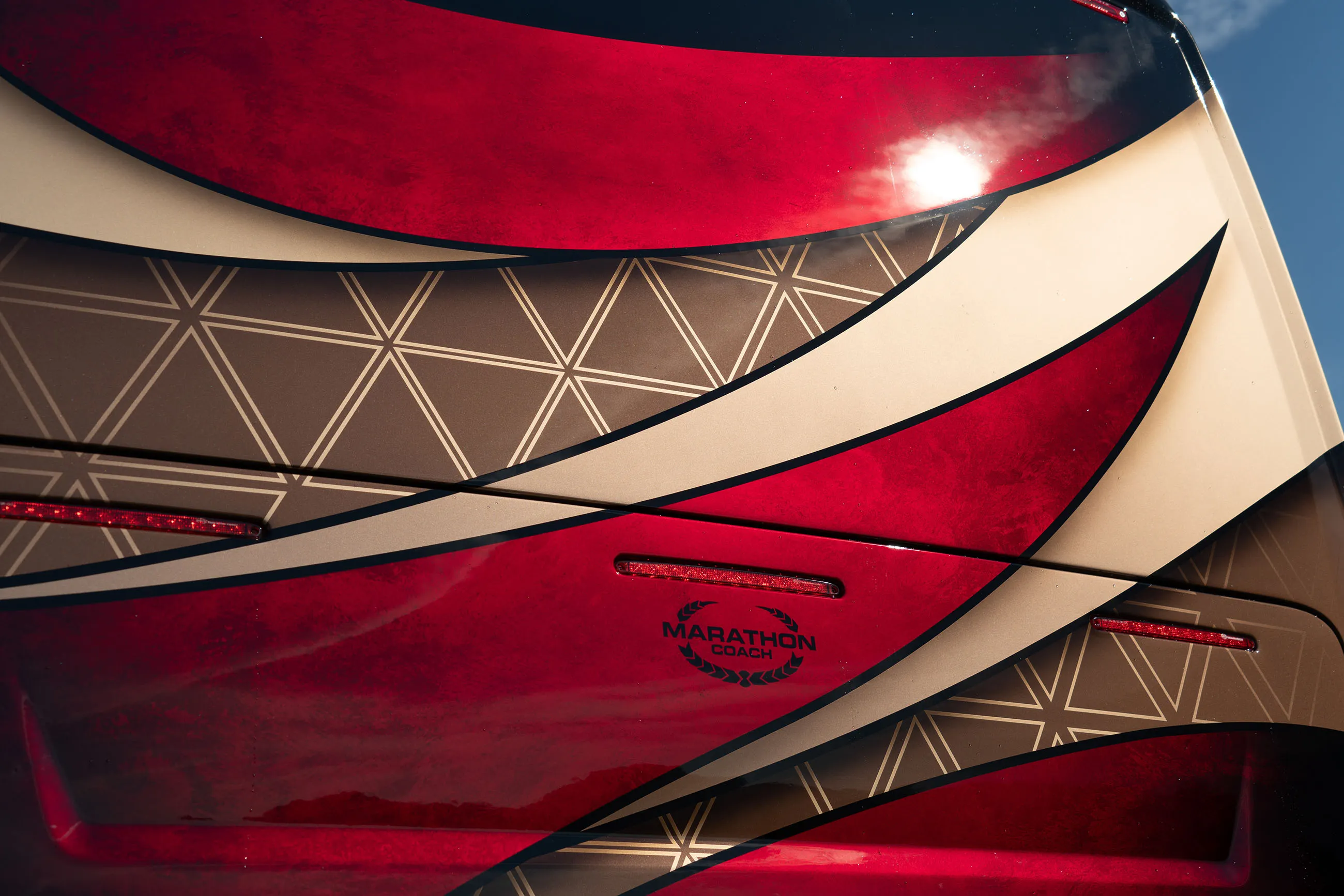 Close-up of a luxury RV exterior featuring red, beige, and brown geometric paint with the Marathon Coach logo.