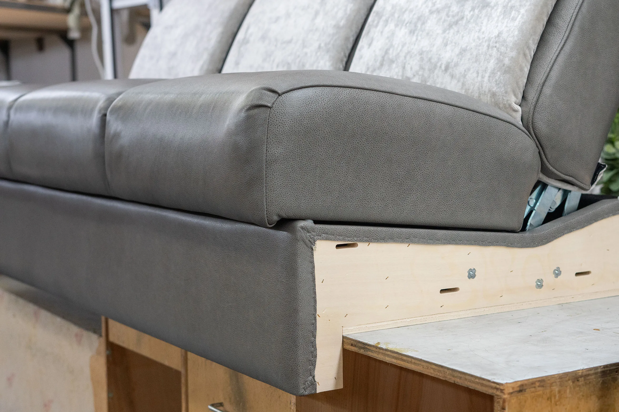 Close-up of a partially upholstered sofa showing grey leather cushions and exposed wooden frame with metal screws.