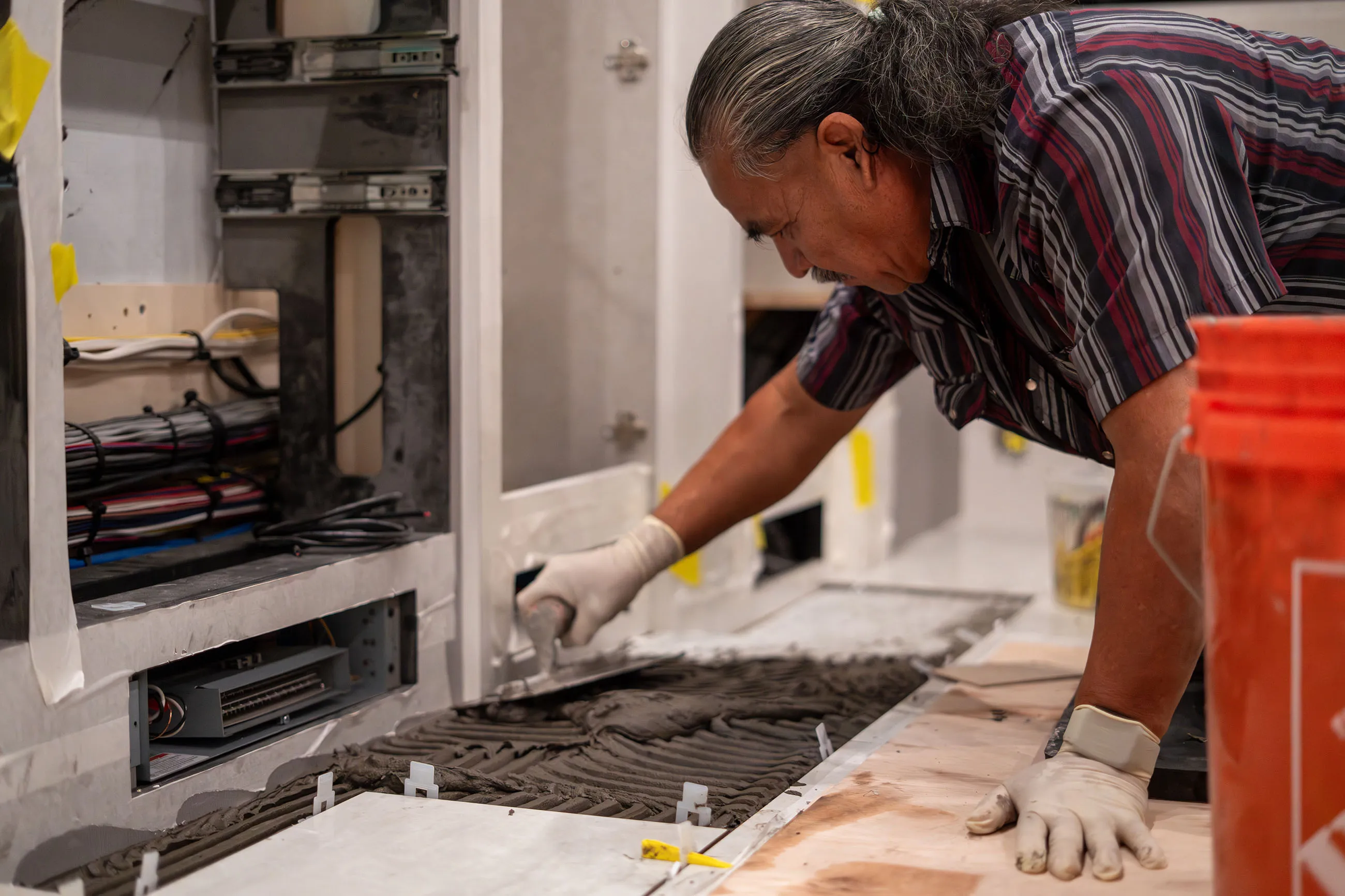 Worker in gloves spreading adhesive on floor preparing to install tiles near electrical wiring.