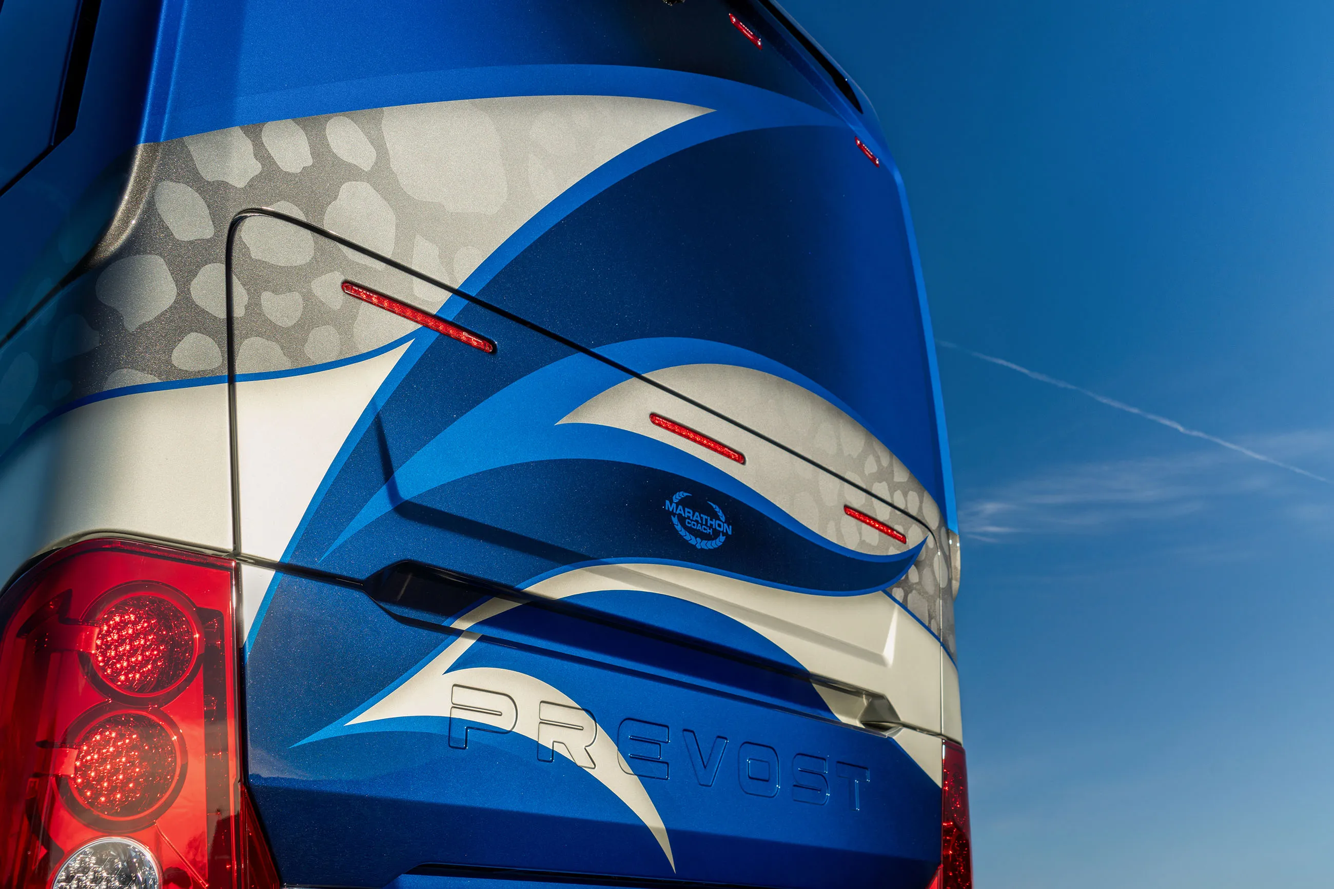 Rear section of a blue and silver Prevost bus with red tail lights and sky background.