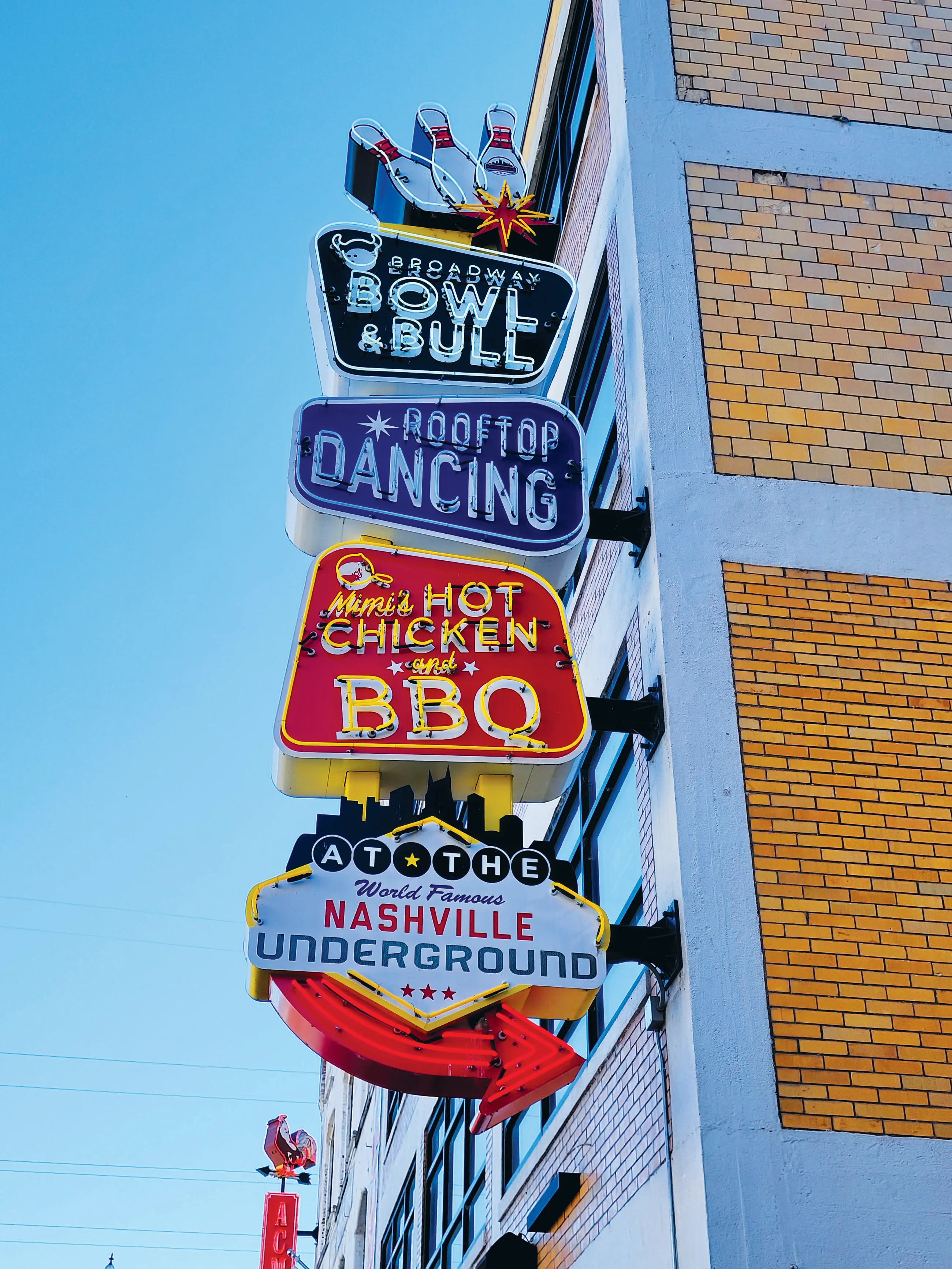 Colorful neon sign on a building advertising Broadway Bowl & Bull, rooftop dancing, Mimi's Hot Chicken and BBQ, and Nashville Underground.