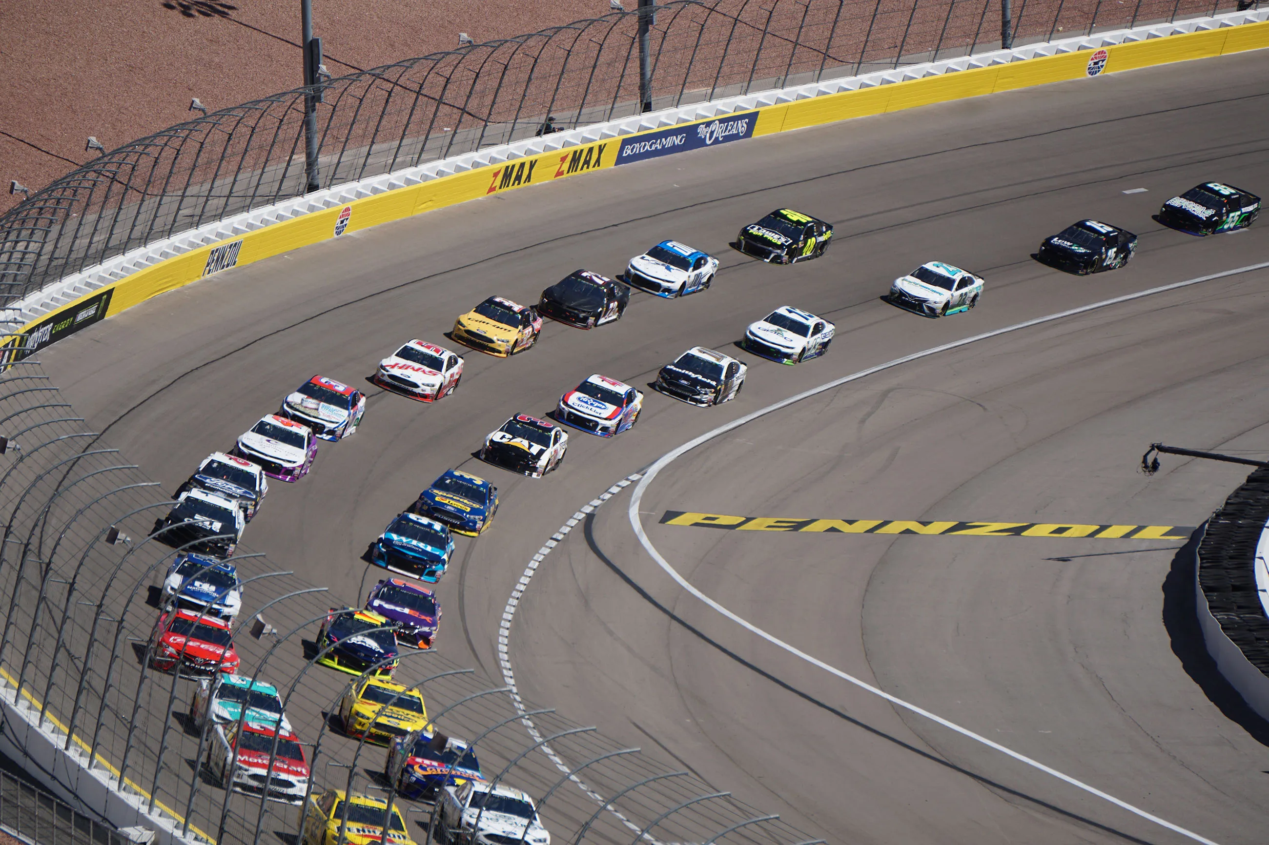 NASCAR stock cars racing on banked track curve with yellow Pennzoil advertisement on asphalt.