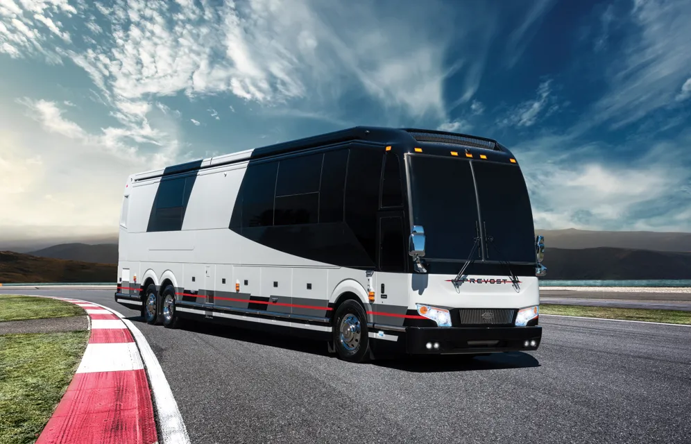 Modern long black and white coach bus on a curved road with cloudy sky and mountains in the background.
