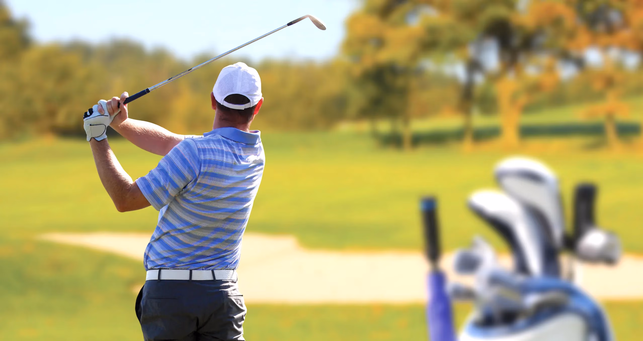 A golfer hitting an approach shot over a green side bunker