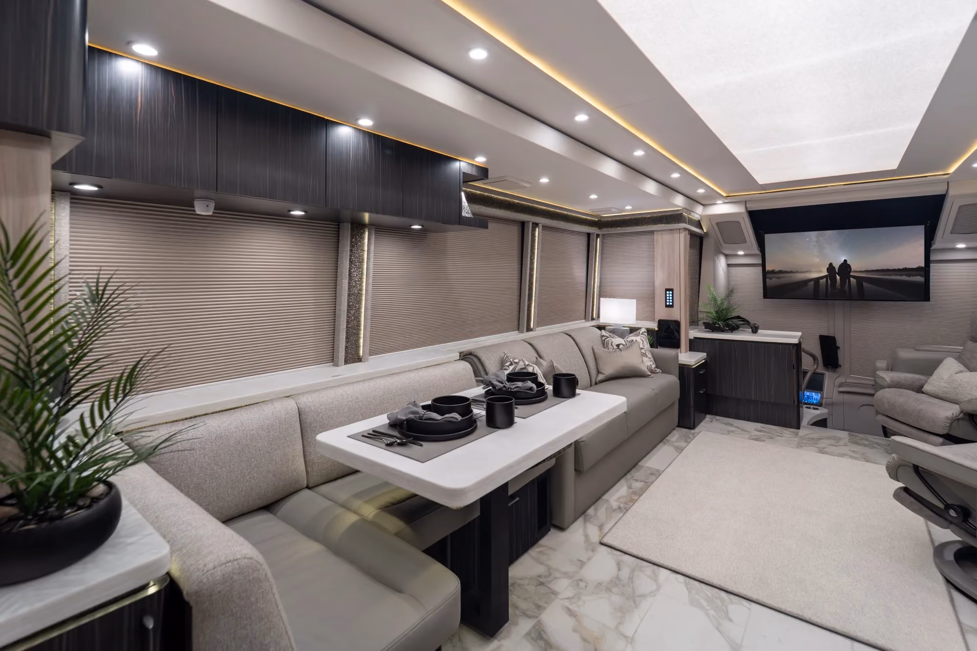 Modern interior of 2027 luxury Marathon Coach #1426 with a grey leather armchair, a dining table with bench seating, and decorative accents.