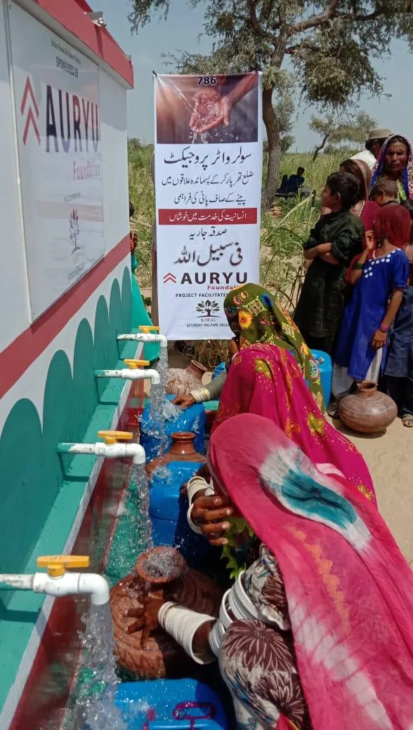 Women in traditional colorful clothing collecting water from multiple taps installed on a solar water project in a rural outdoor setting.