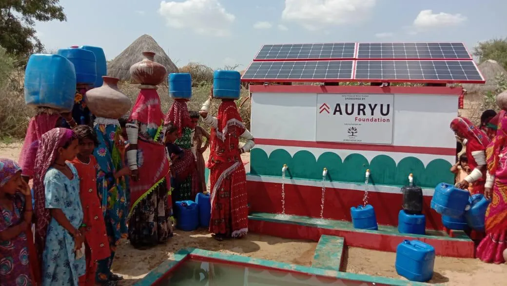 Group of women in colorful traditional clothing collecting water from a solar-powered water tap system in a rural area.