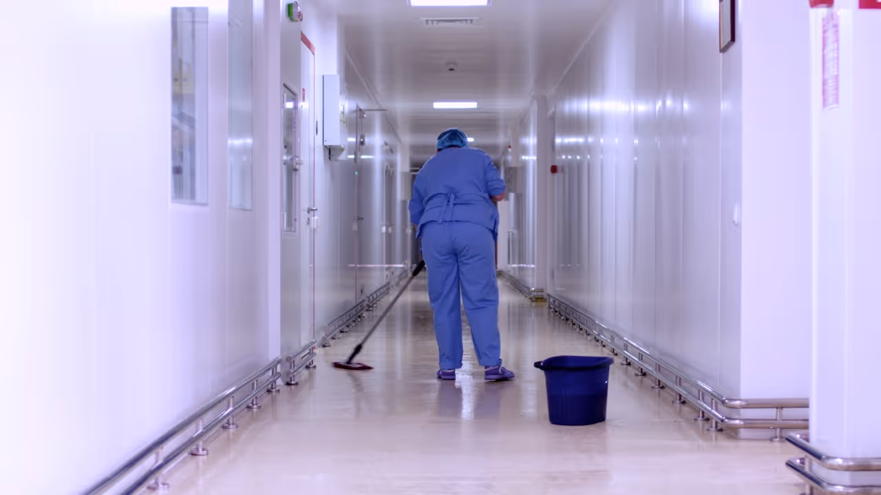 Person in blue scrubs mopping a clean, long hallway floor