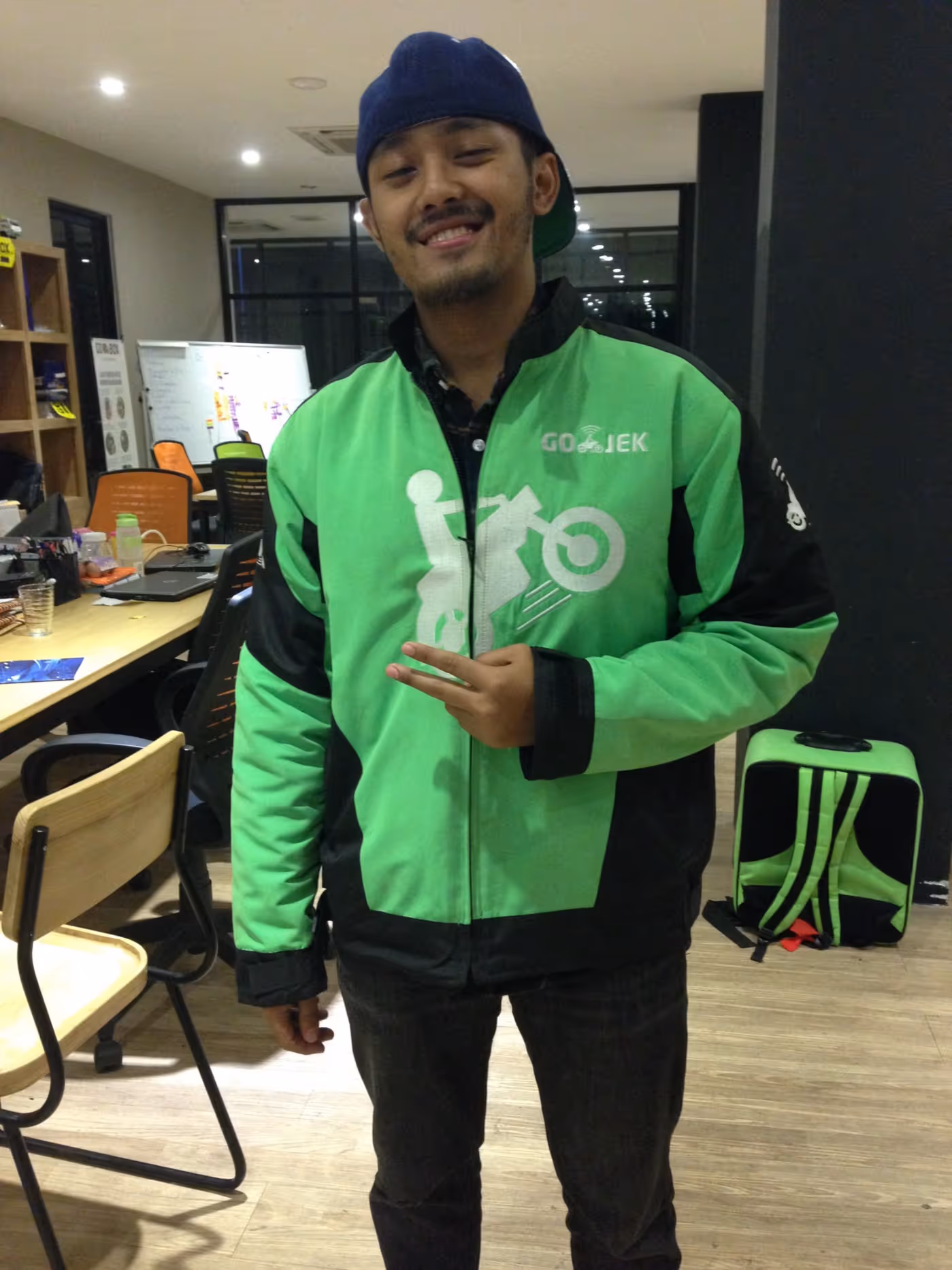 Picture of Man smiling wearing Gojek uniform with tables and chairs in background 