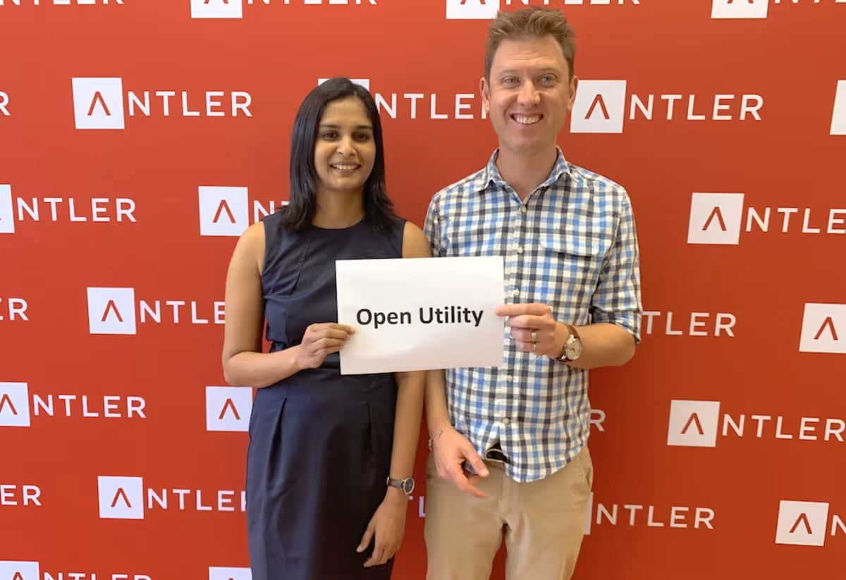 Aswathi Thandassery and her co-founder Dan Linsell hold Open Utility sign in front of Antler background 