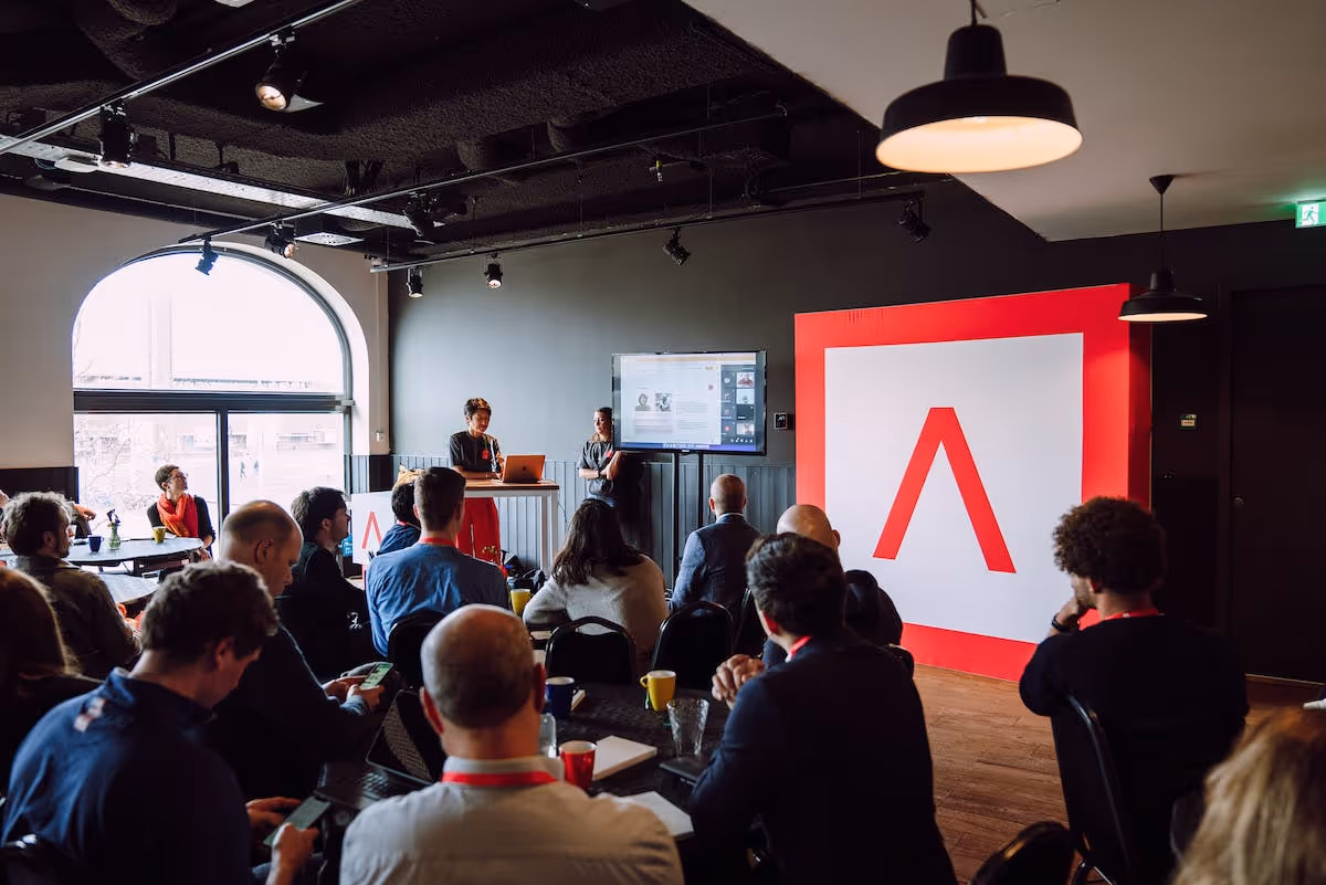 Audience sitting down watching presentation in Amsterdam with large Antler Logo sign 