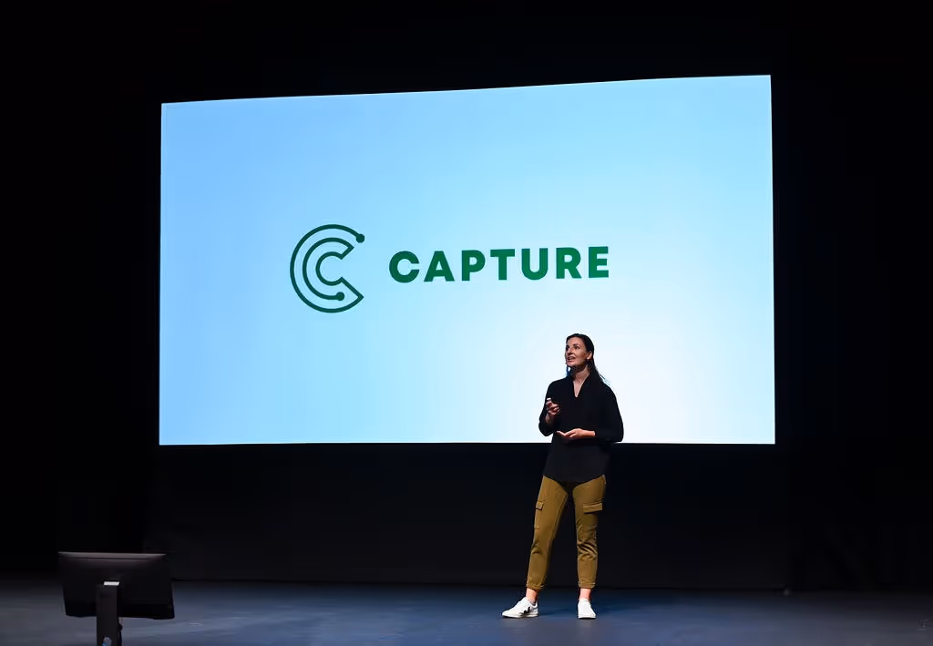 Co-Founder of Capture Josie Stocker does presentation on stage with Capture logo on screen behind her t