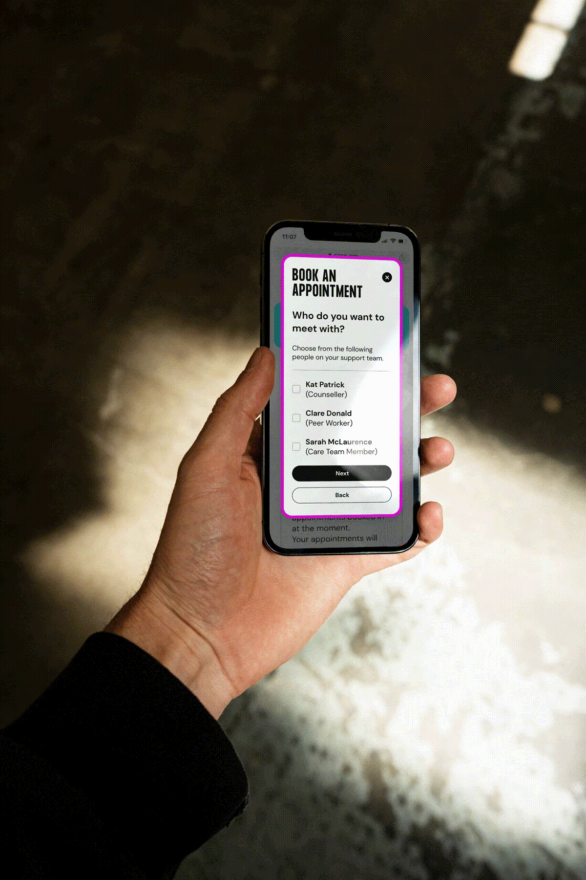 A hand holding a phone showing the SANE care platform, with a welcome message guiding the user through personalised onboarding steps.