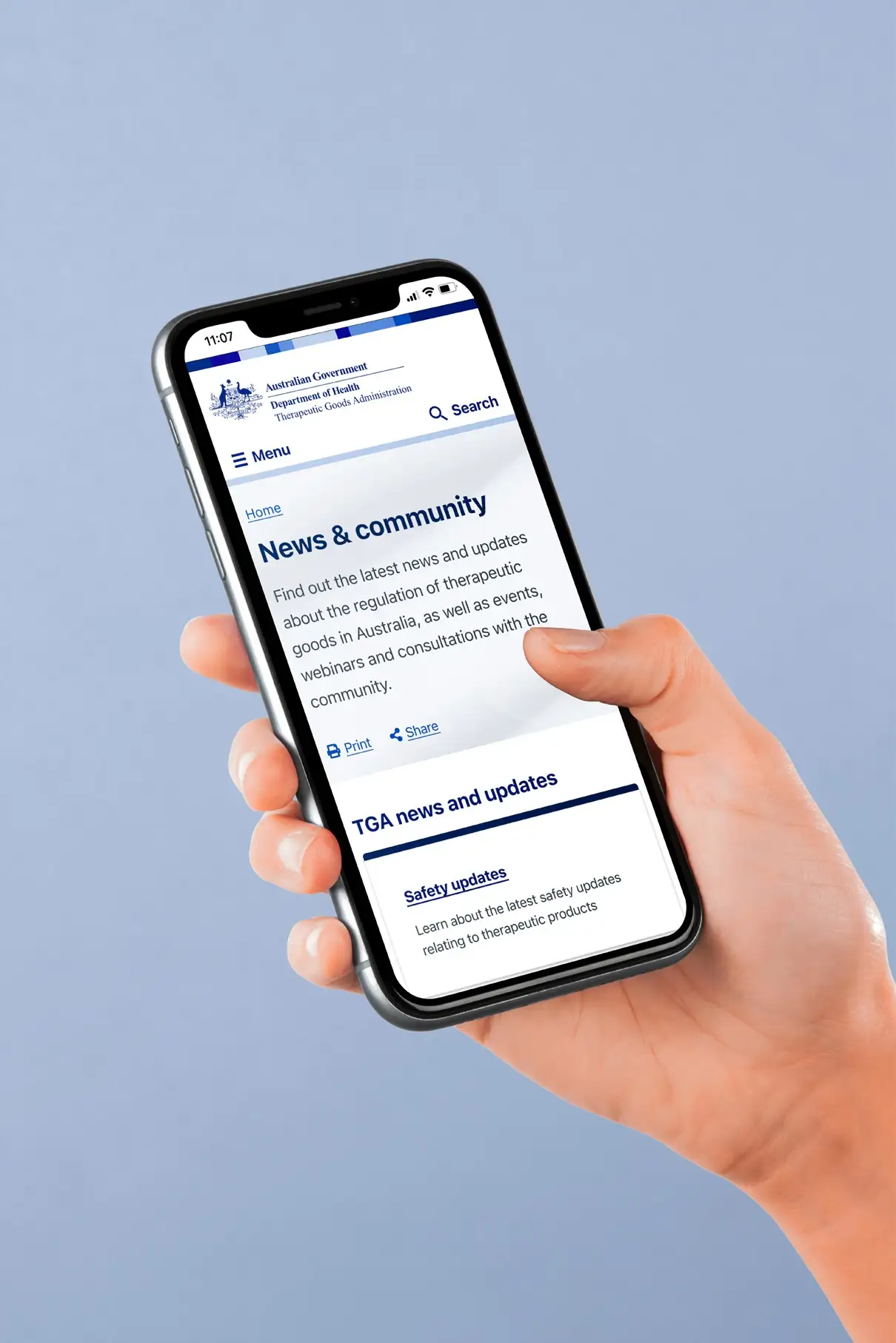Hand holding a mobile phone displaying the TGA “News & community” page, demonstrating mobile responsiveness of the redesigned site.