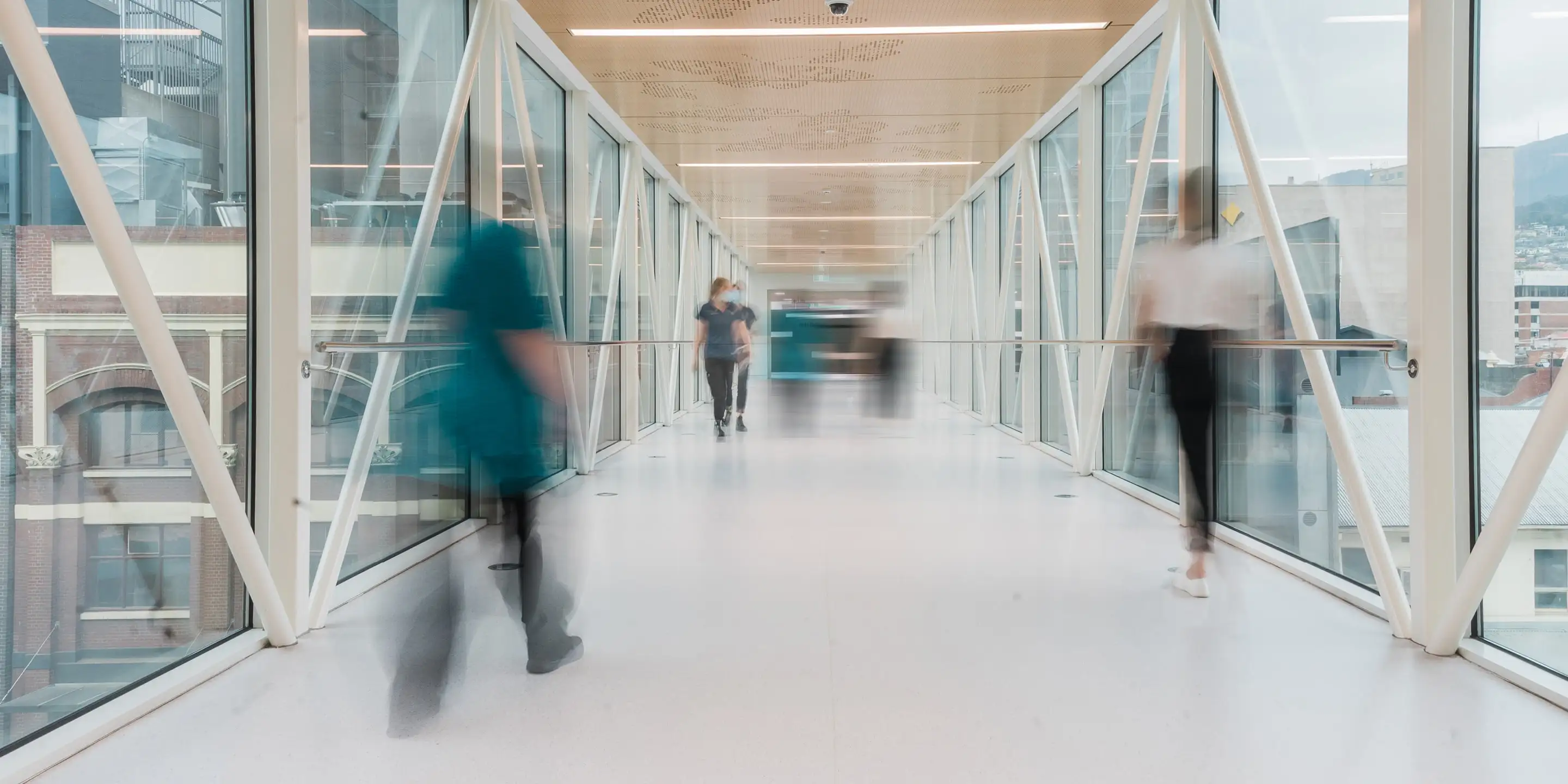 Blurry figures of people walking in a modern glass corridor with a cityscape visible outside.