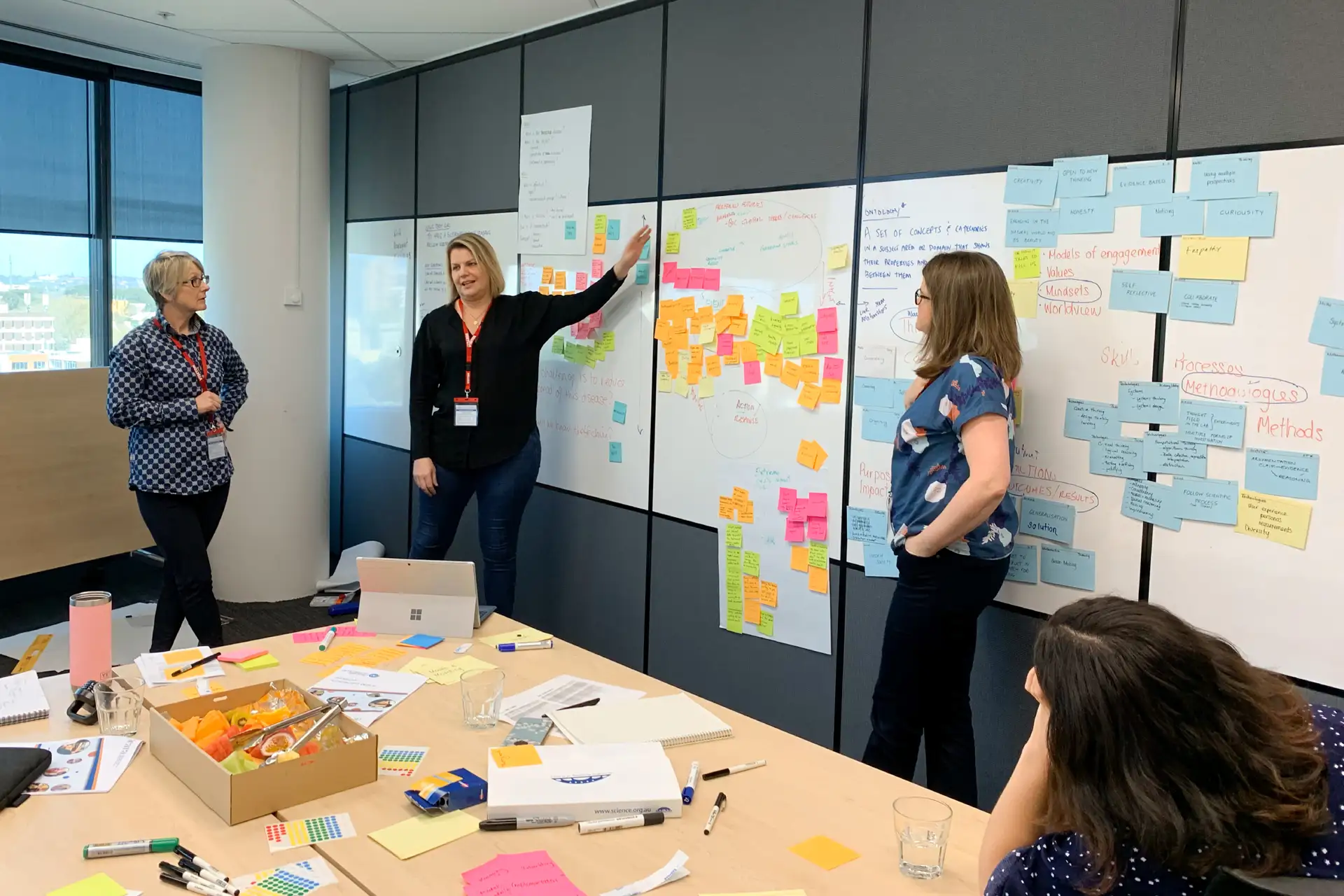 Alt text: A wall covered with printed diagrams and sticky notes showing research insights, journey maps, and planning frameworks for an education project.