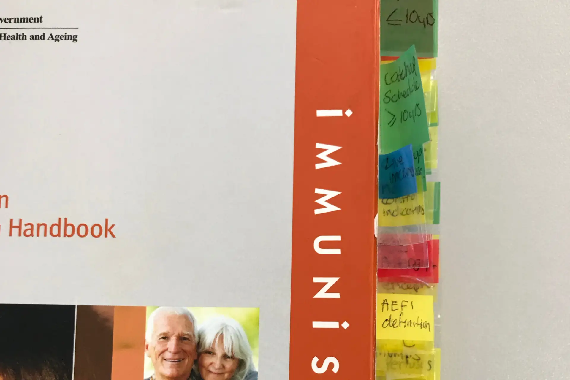 Close-up of a printed Immunisation Handbook with numerous coloured sticky notes marking key sections.