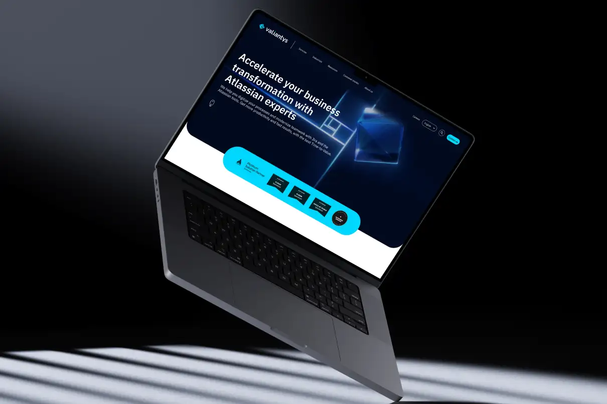 A floating laptop against a dark gradient background displaying the Valiantys website homepage with a dark UI.