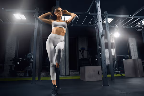 Fit woman in white athletic wear doing standing abdominal exercises in a gym.