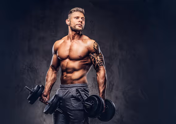 Muscular man with a tattoo lifting two dumbbells against a dark textured background.