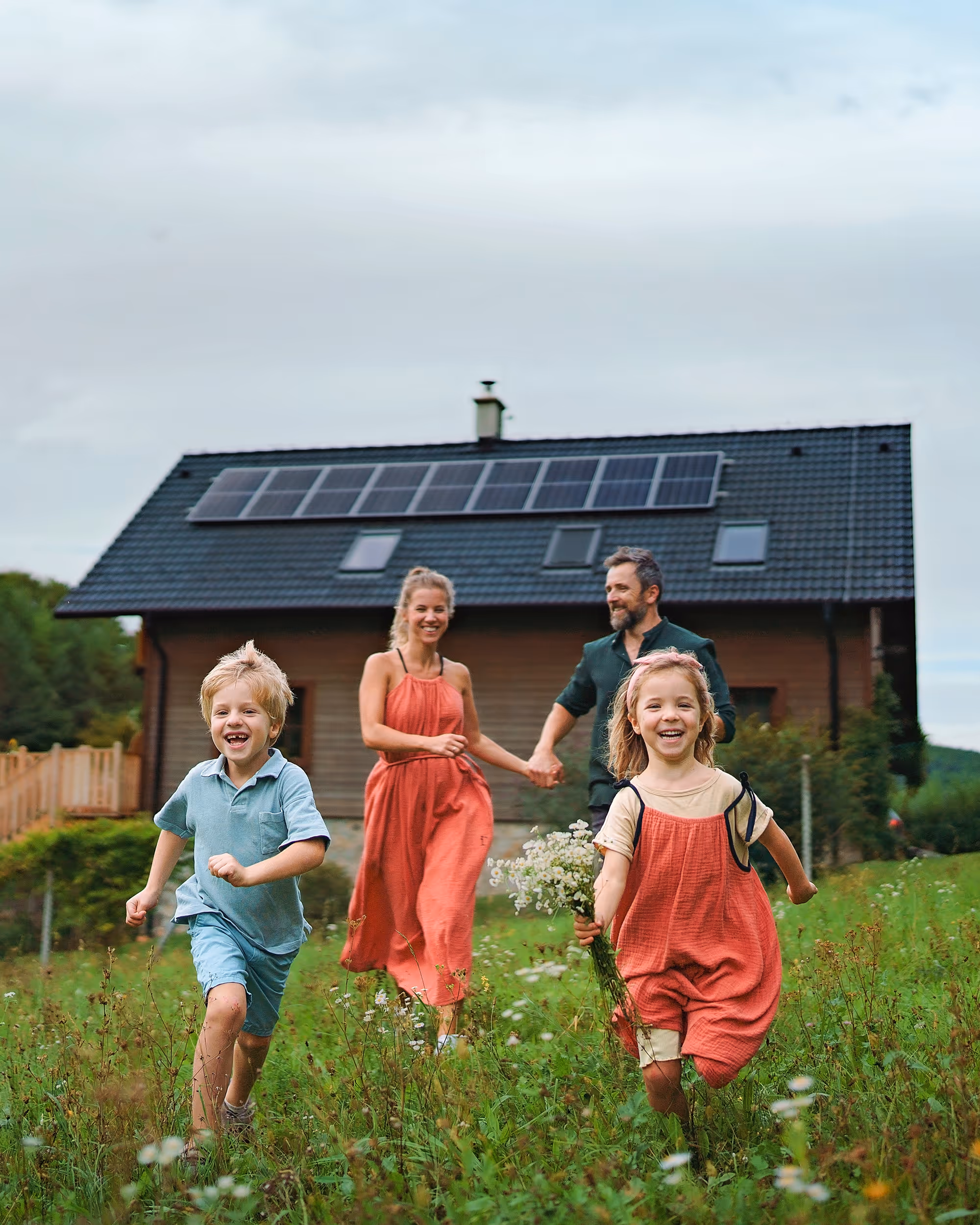 A family in a field in front of a house with solar panels. Two children running away from the house.