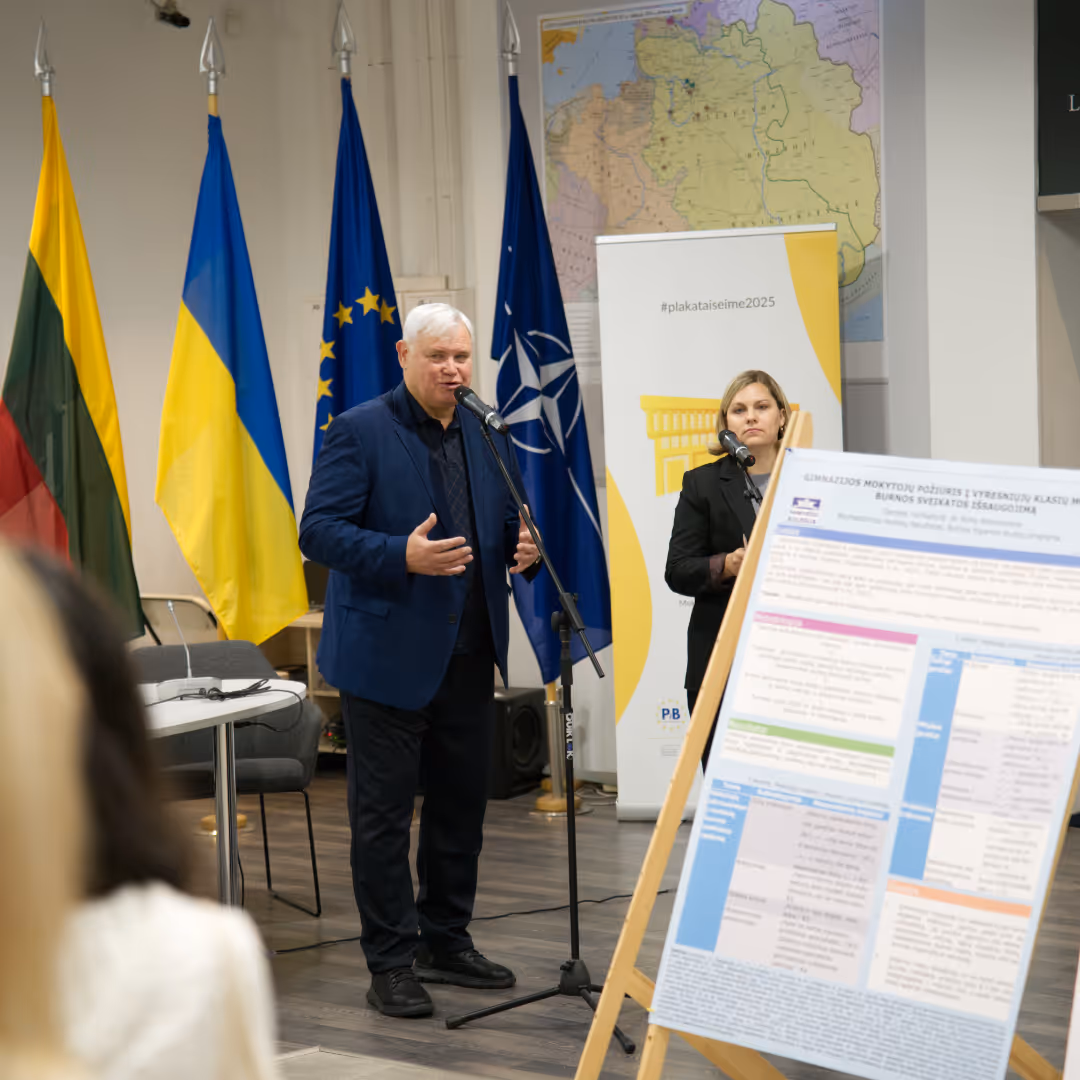 Two speakers at microphones in a room with flags of Lithuania, Ukraine, the European Union, and NATO in the background, and a presentation poster on an easel.