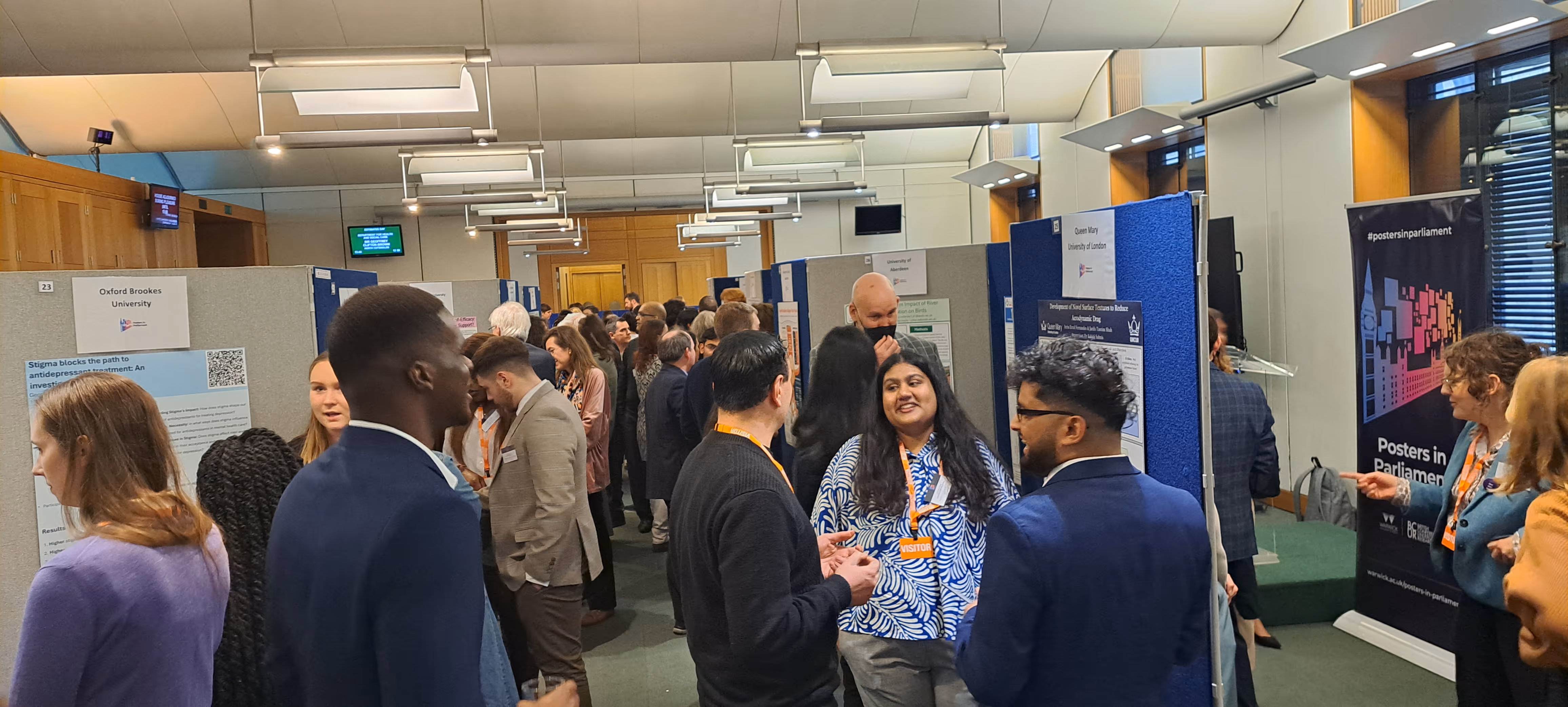 Two speakers at microphones in a room with flags of Lithuania, Ukraine, the European Union, and NATO in the background, and a presentation poster on an easel.