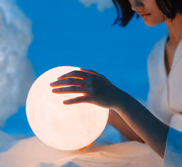 Person gently holding a glowing spherical light resembling the moon against a blue background.