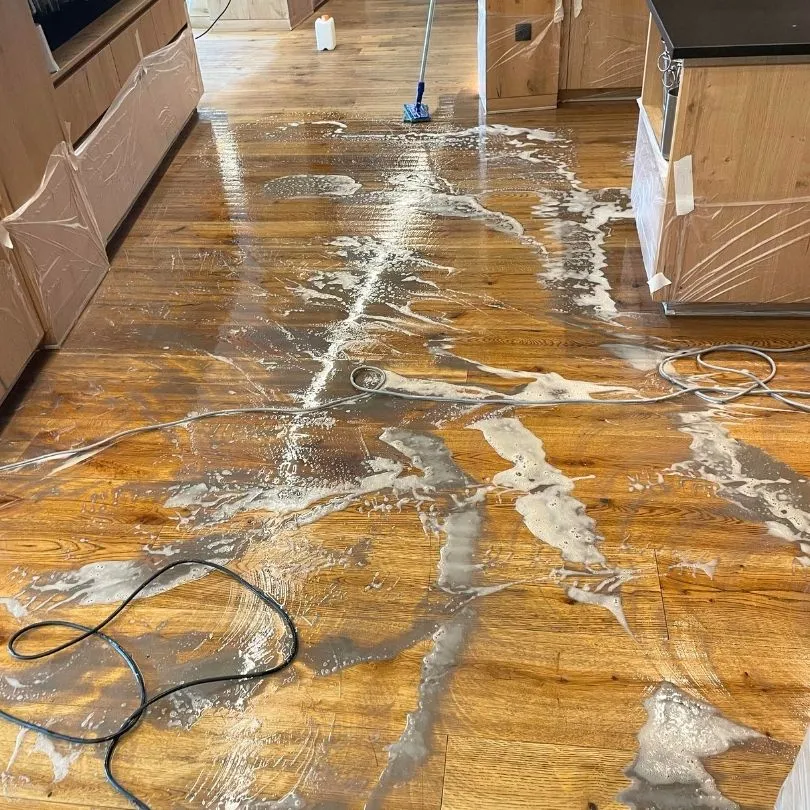 Nasser, eingeschäumter Holzboden in einer Küche mit einem Mopp und Kabeln auf dem Boden.
