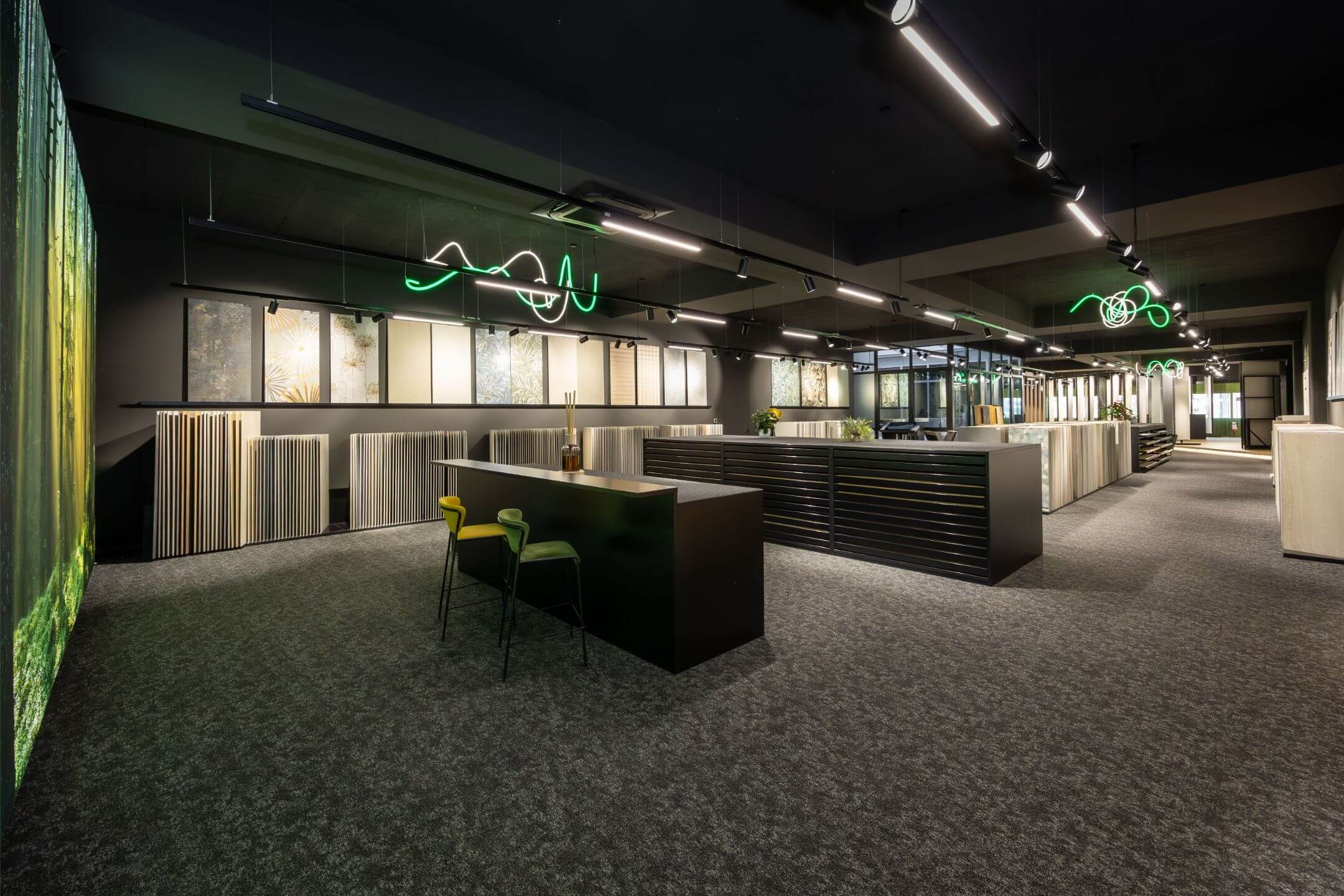 Modernes, großzügiges Showroom-Interieur mit dunkler Decke, Neonlichtern, verschiedenen Wandpaneelen und Stehtischen mit bunten Stühlen.