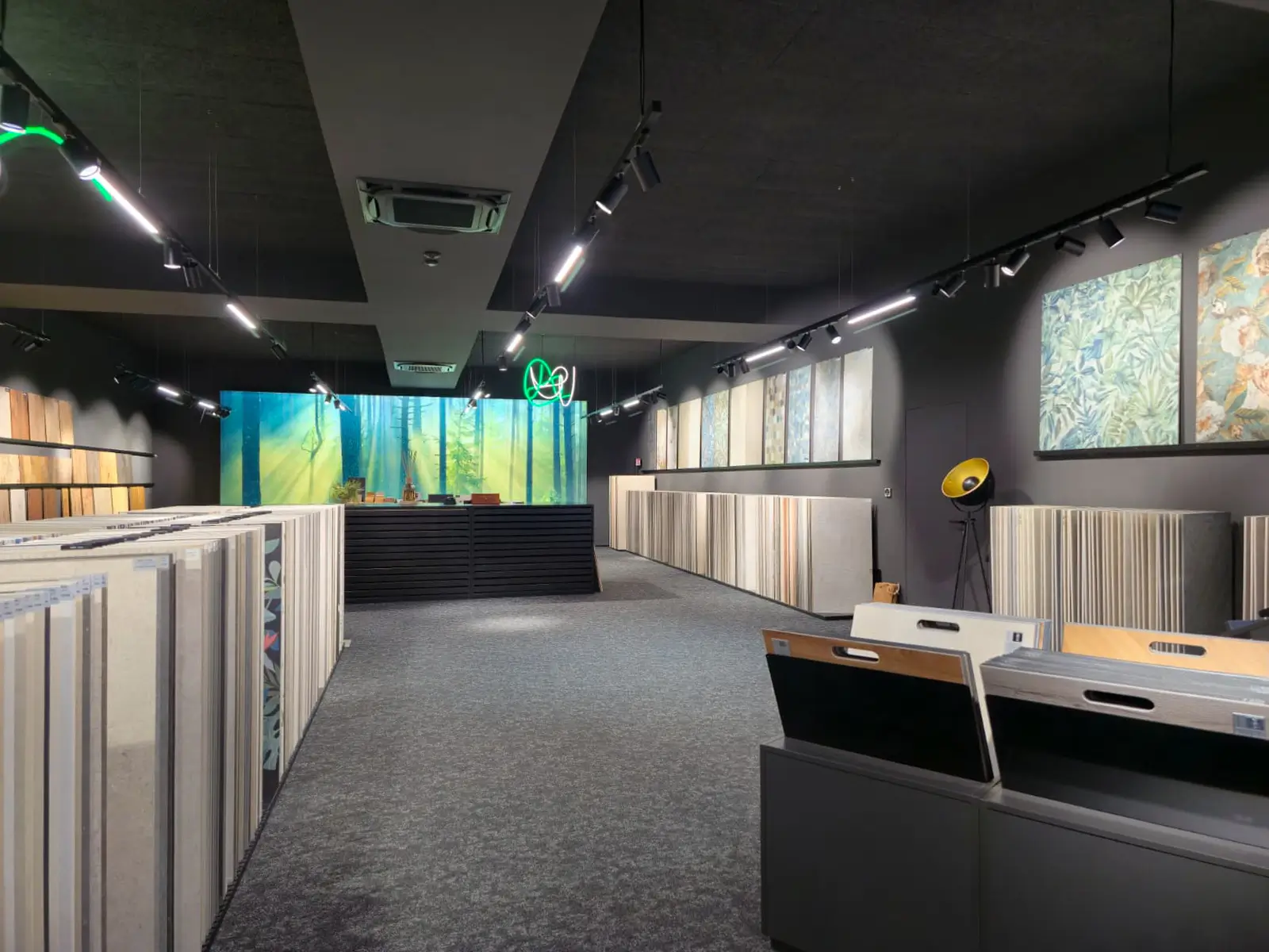 Modernes Showroom-Interieur mit Boden- und Wandfliesenmustern auf Display-Ständern und leuchtendem Waldmotiv im Hintergrund.