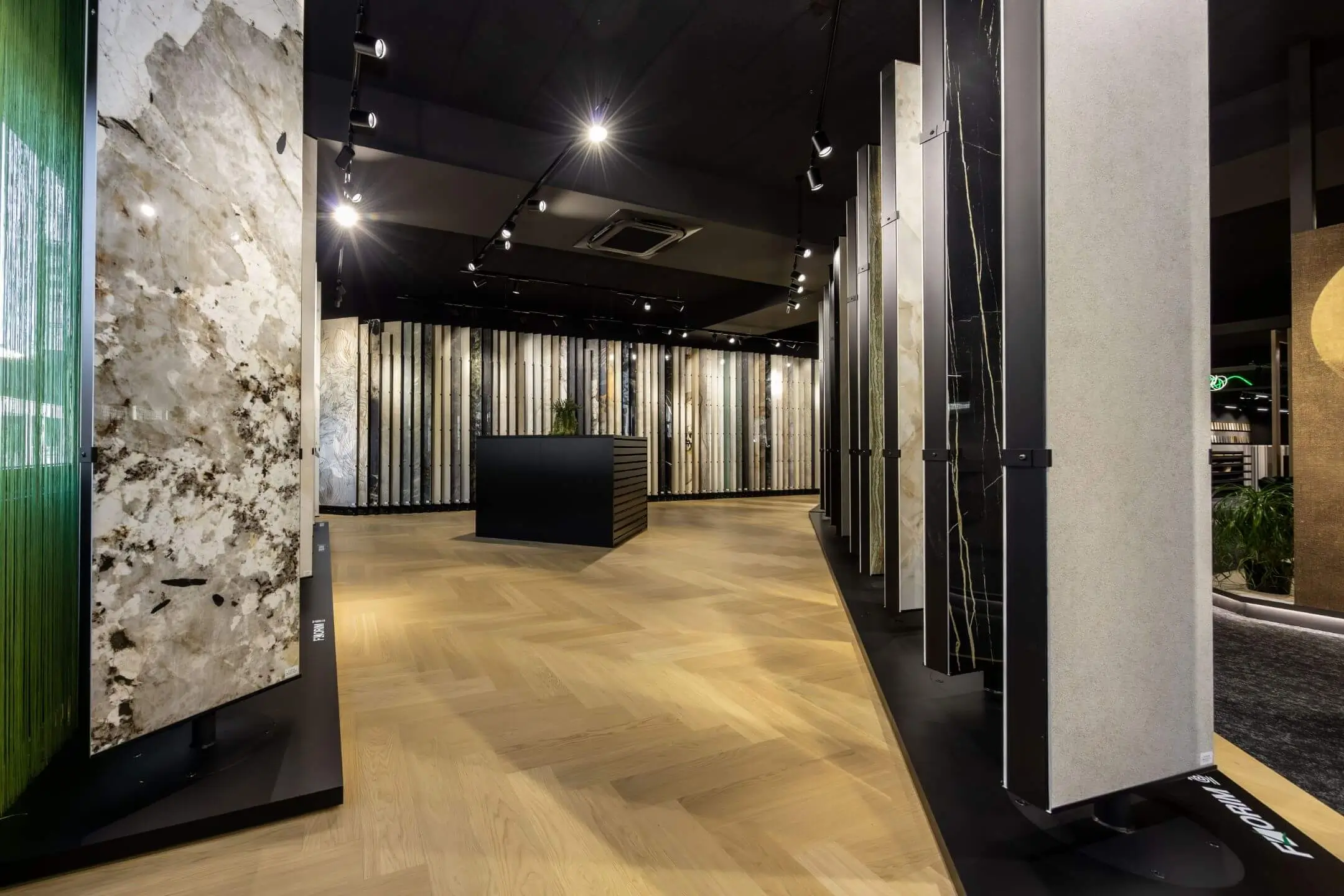 Moderne Ausstellung mit großen Mustertafeln aus verschiedenen Steinen und Materialien in einem gut beleuchteten Raum mit Holzparkettboden.