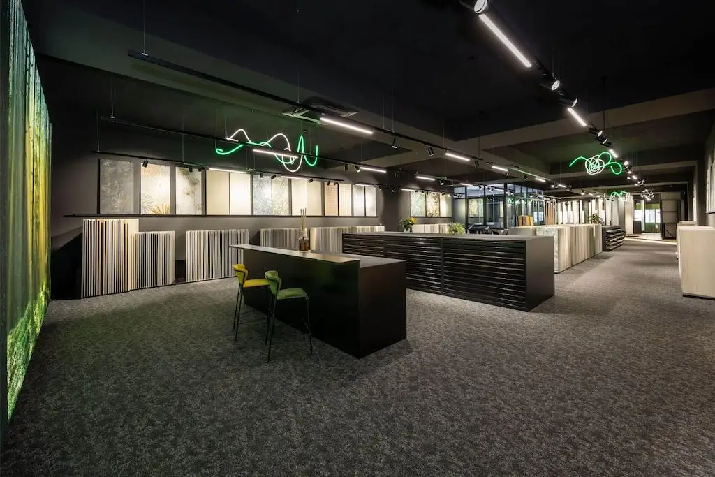 Moderner Showroom mit Teppichboden, einem langen schwarzen Tisch mit zwei Stühlen und verschiedenen großen Musterplatten an den Wänden.