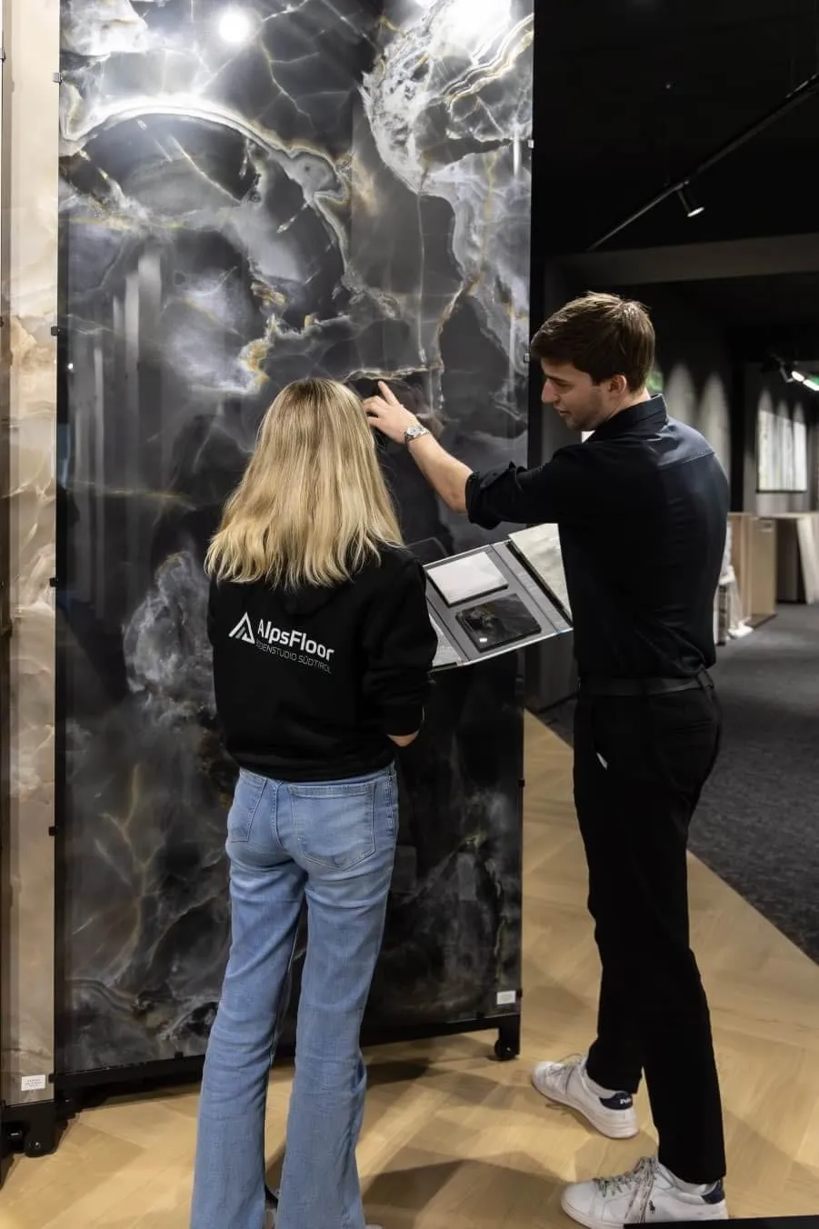 Zwei Personen betrachten und besprechen eine große schwarze Marmorplatte in einem Showroom für Bodenbeläge.