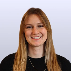 Vrouw met lang blond haar lacht naar de camera, draagt een zwarte trui en een dunne ketting.