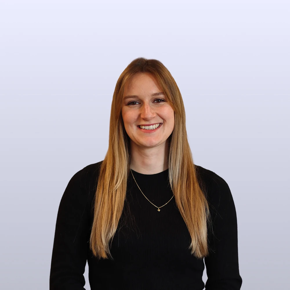 Vrouw met lang blond haar en zwarte trui, glimlachend voor een lichte achtergrond.