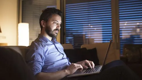 Mann sitzt auf Couch und schaut in Laptop