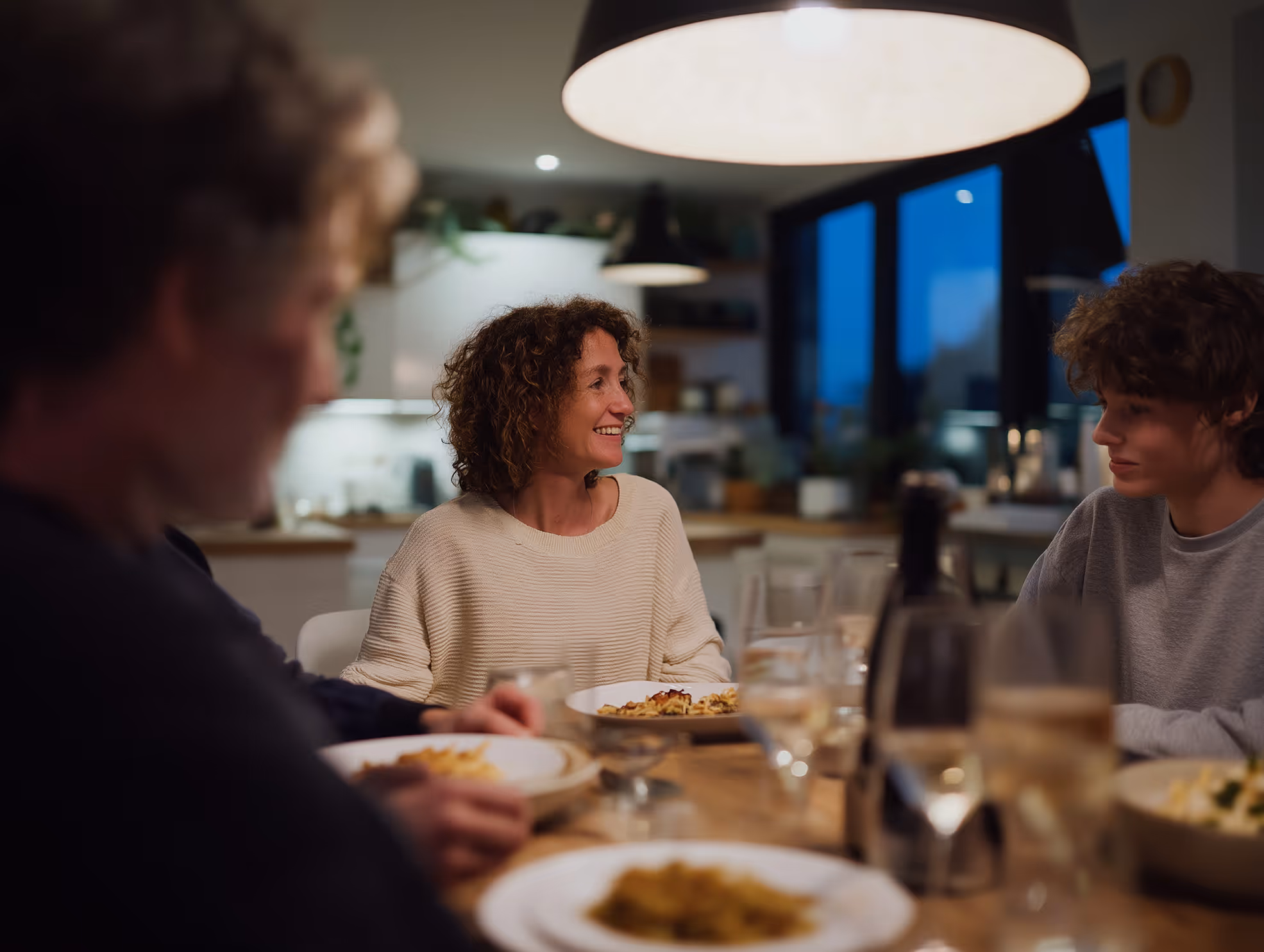 Eine Familie sitzt abends gemeinsam an einem gedeckten Esstisch in einer modernen Küche.