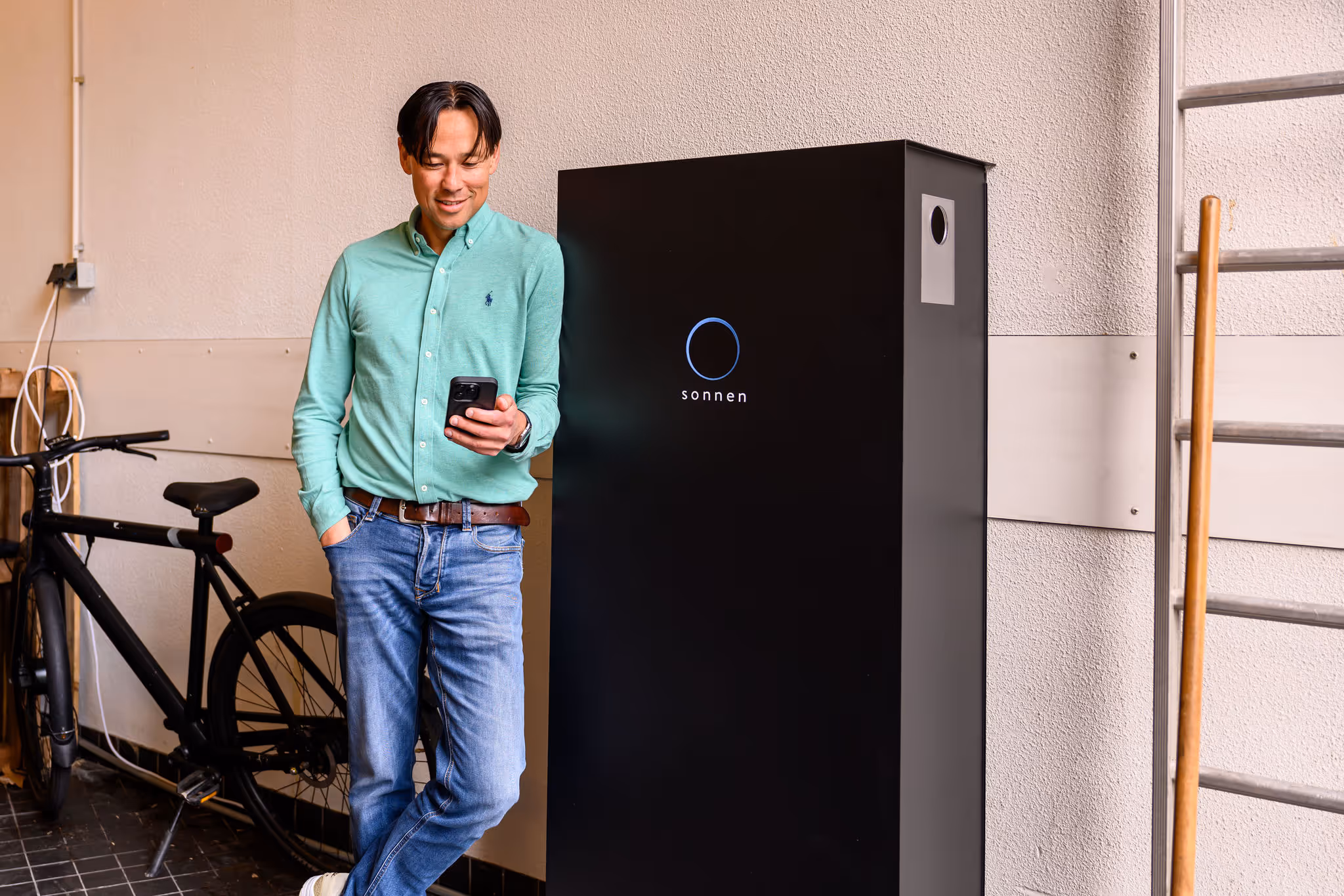 A smiling man with a smartphone in his hand leaning on a sonnenBatterie