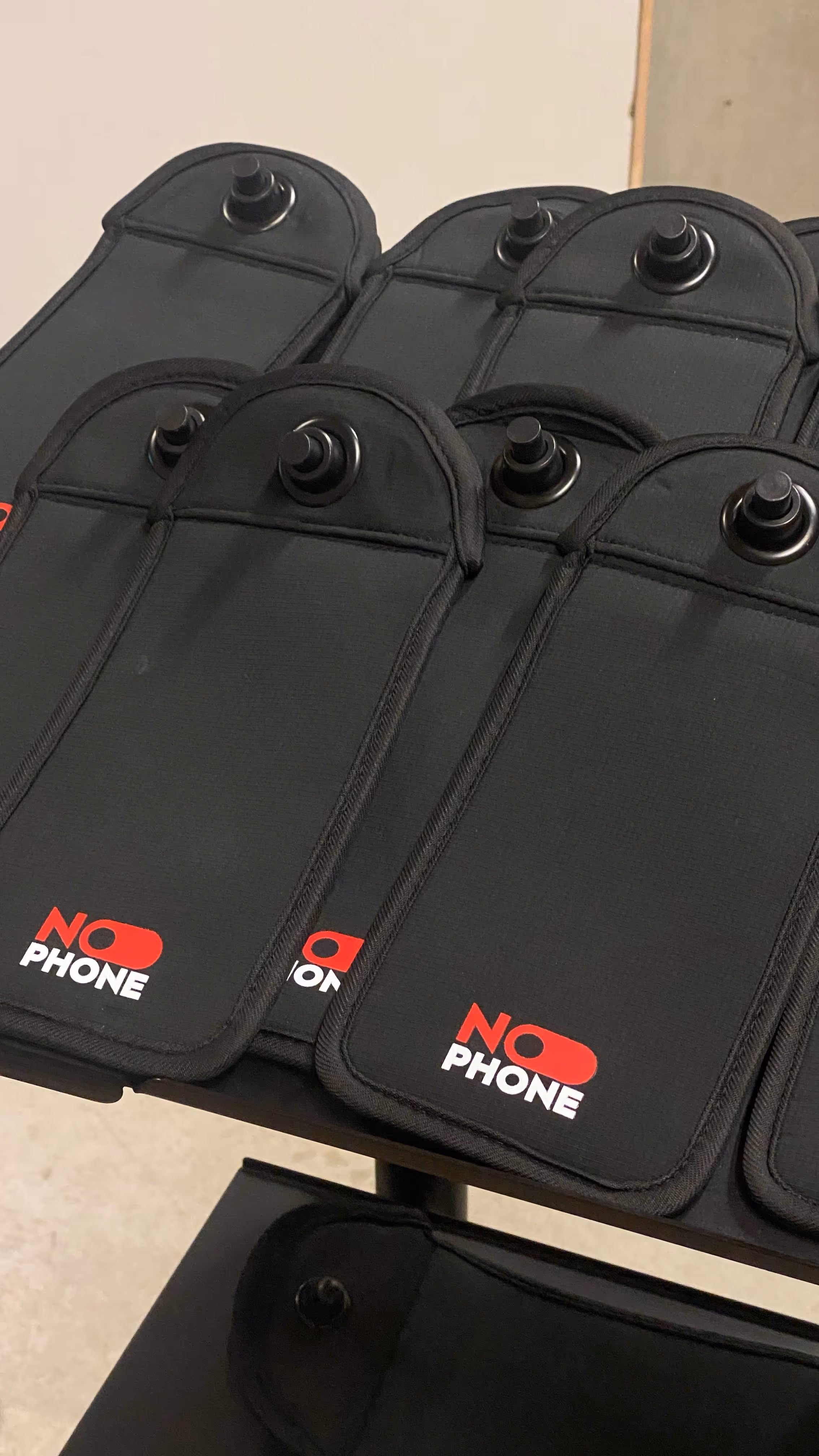 Lot de pochettes NoPhone noires avec système de verrouillage, disposées sur une table, destinées à réguler l’usage des smartphones en milieu scolaire
