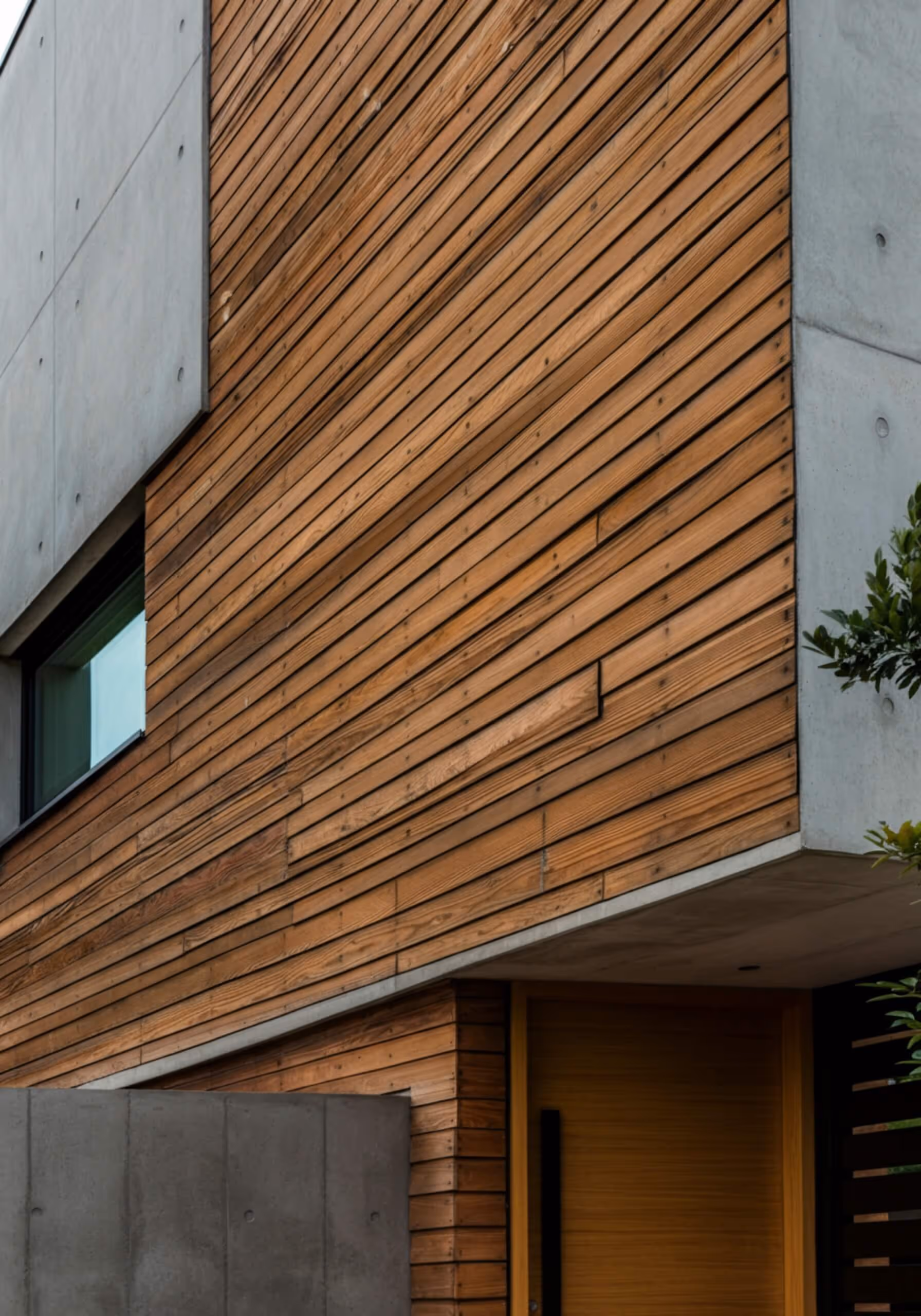 Modern building facade with horizontal wooden paneling, concrete sections, and a small window.
